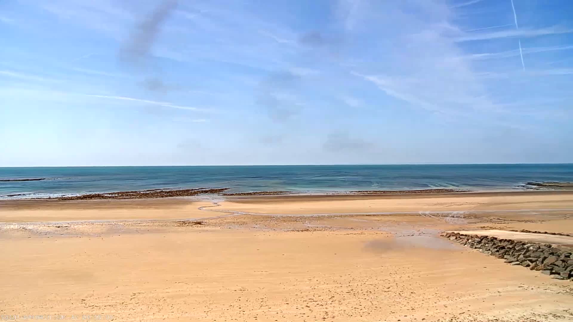 A sandy beach stretches to a calm, teal ocean under a mostly sunny sky with a few scattered clouds.