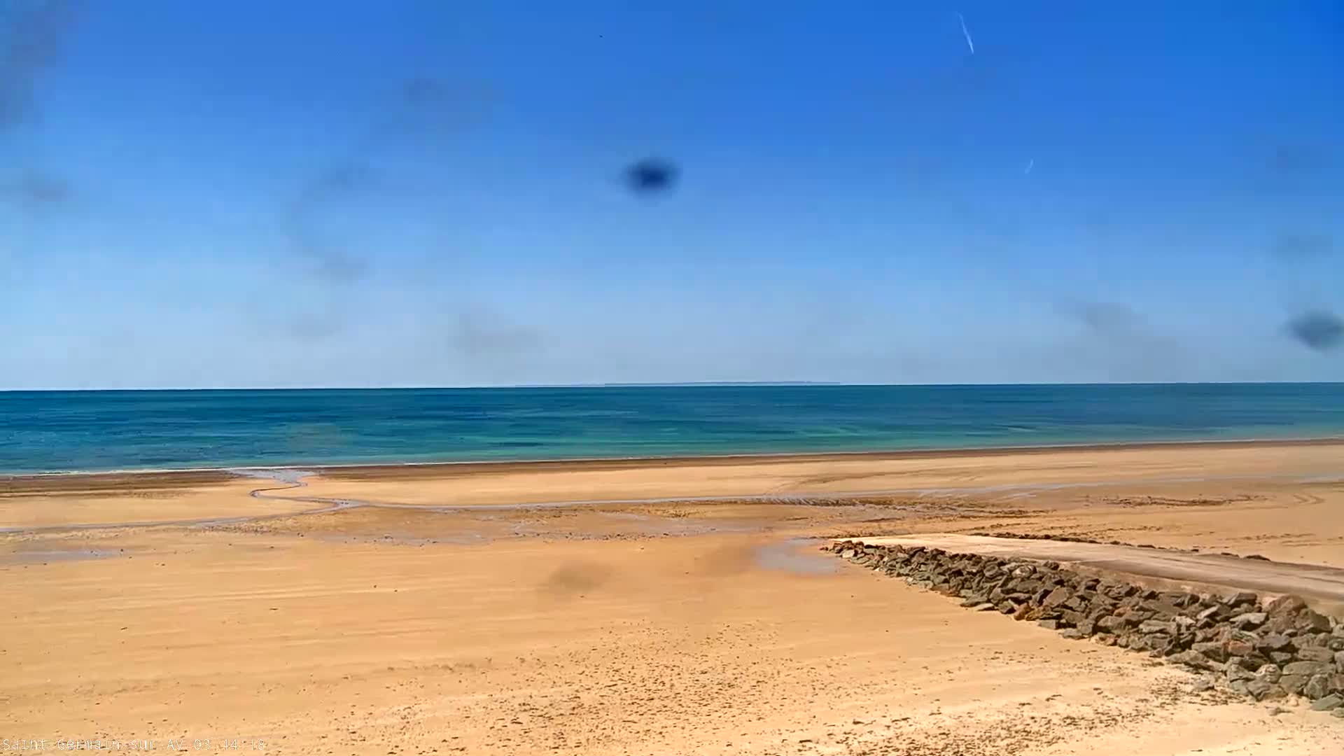 A sandy beach stretches to a calm, turquoise ocean under a clear blue sky.