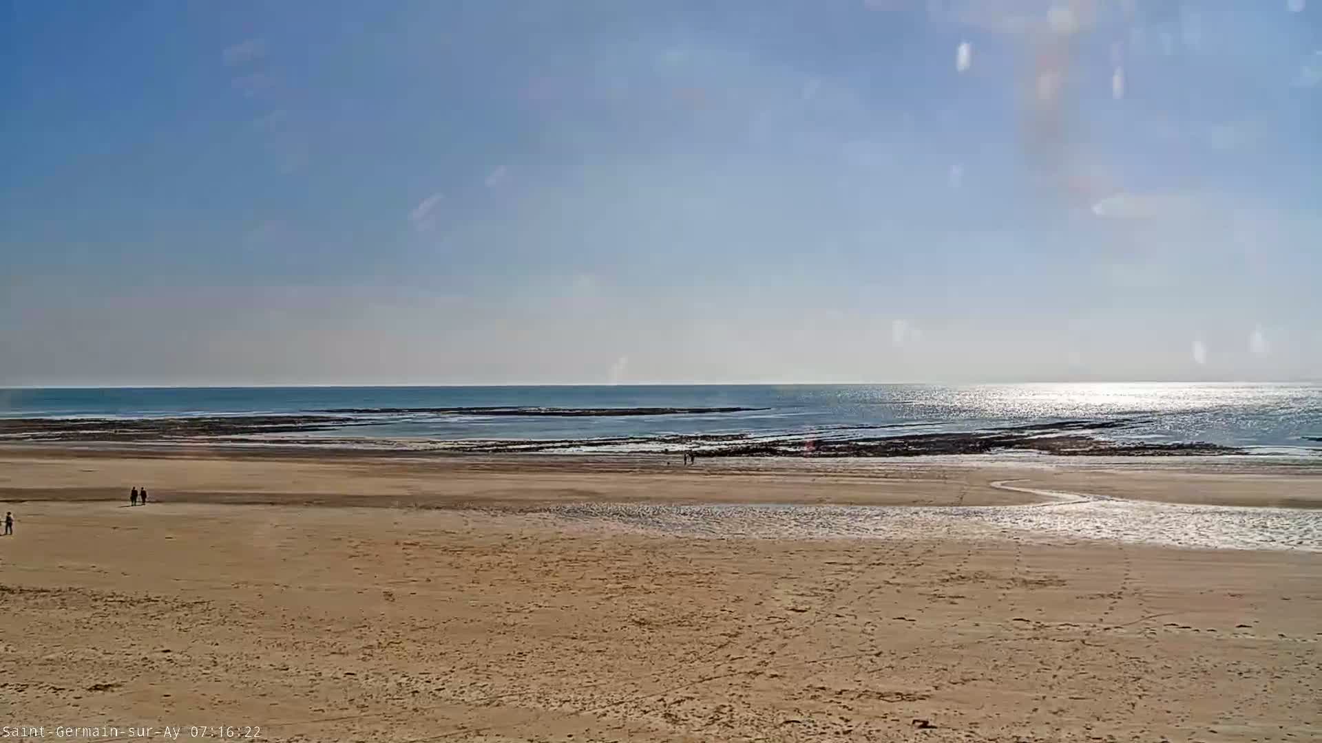 A sandy beach stretches to a calm ocean under a clear blue sky.