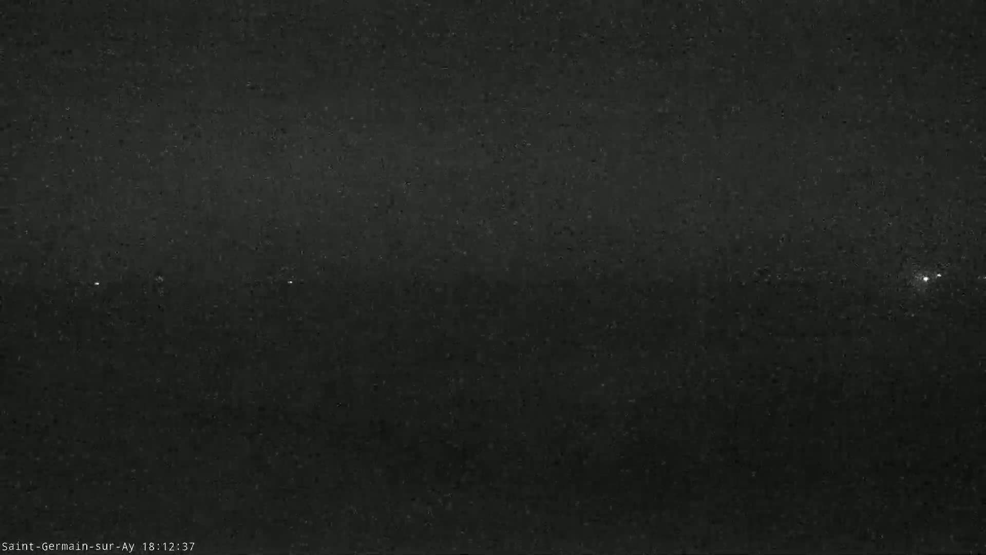 A nighttime, grainy image shows a dark sky with a few faint lights visible.