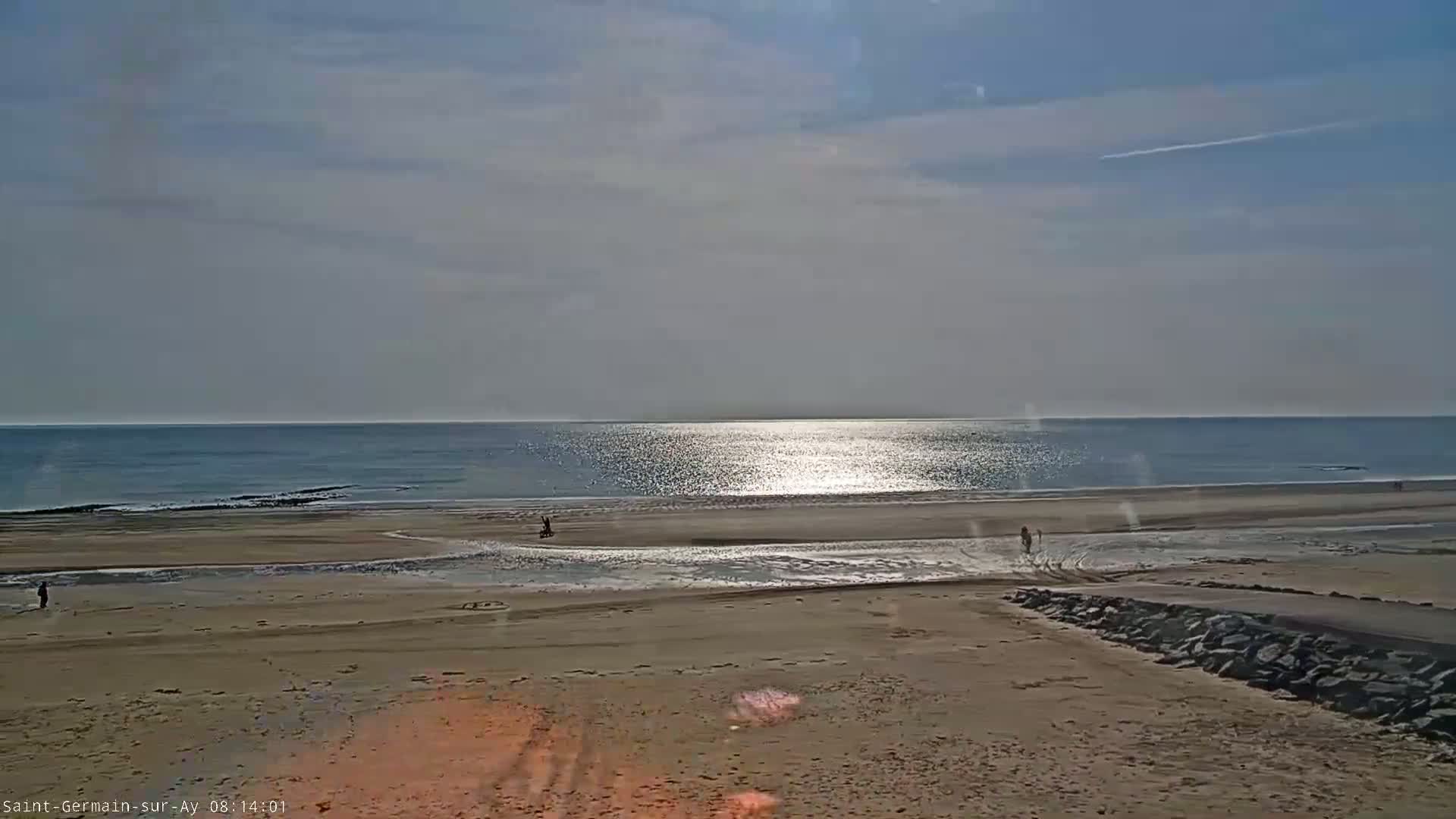 A wide sandy beach stretches toward a calm, sunlit ocean under a mostly clear sky.