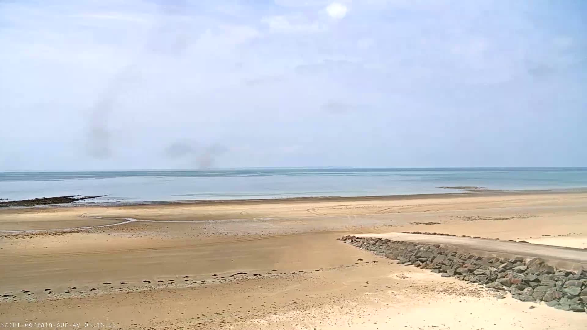 A wide sandy beach stretches to a calm sea under a mostly clear sky.