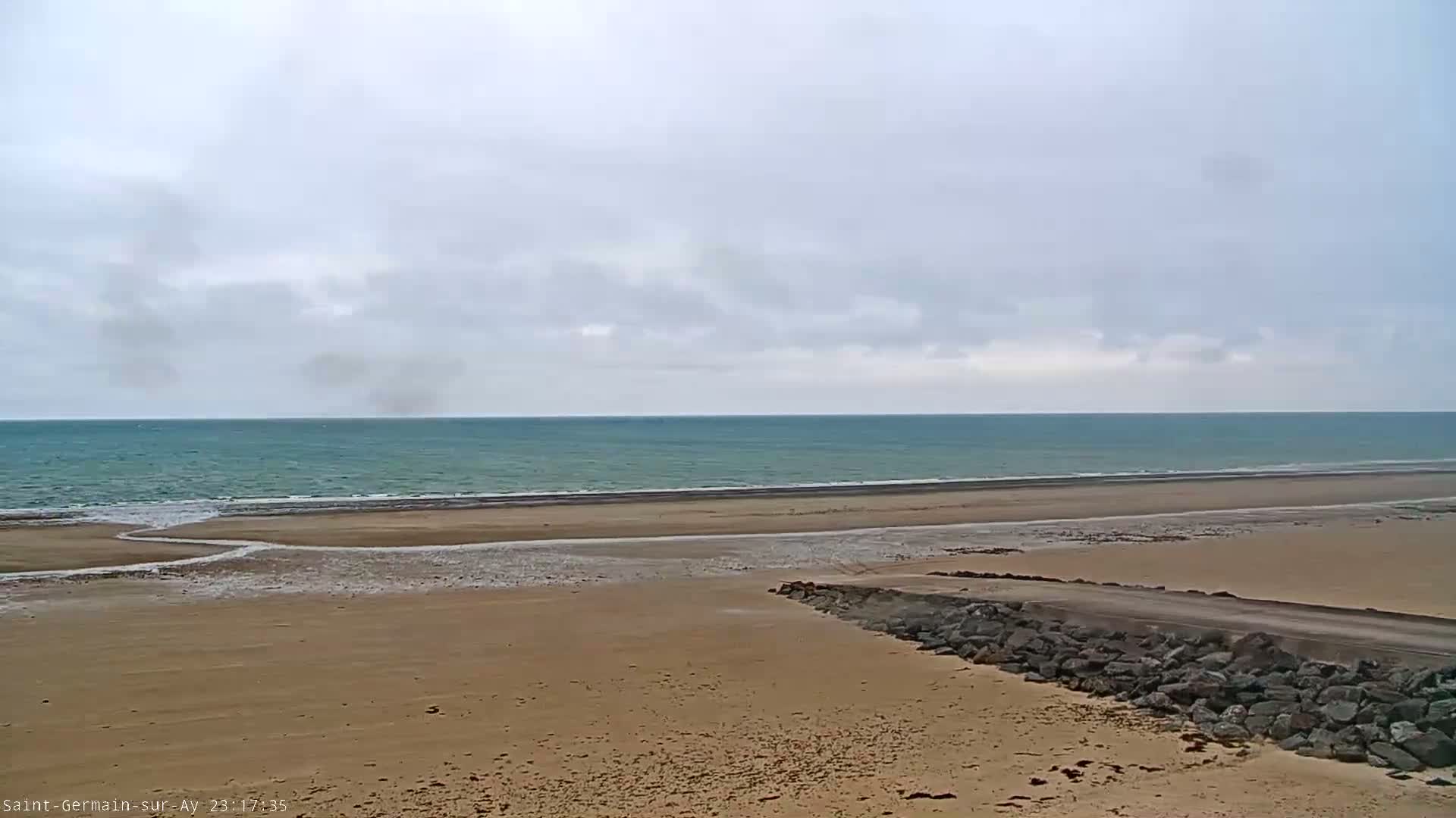 A wide sandy beach stretches to a calm, teal ocean under a cloudy sky.