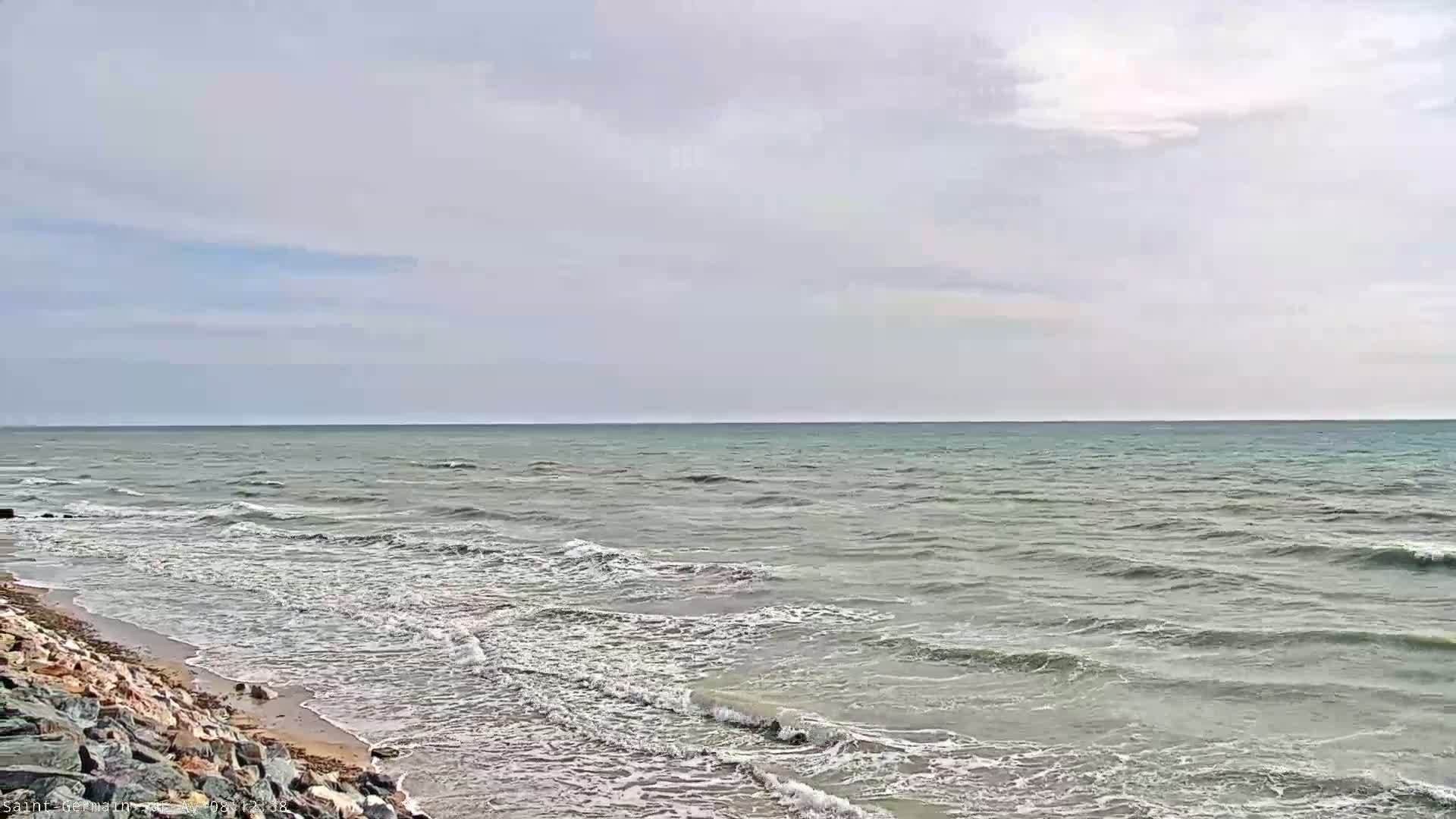 A rocky shoreline meets a sea with small waves under a mostly cloudy sky.