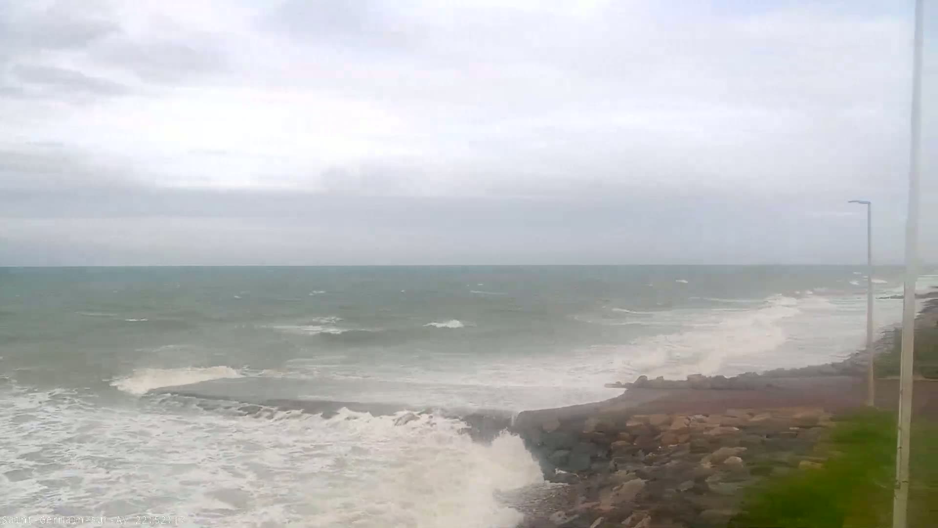 Waves crash against a rocky shore under a cloudy sky.