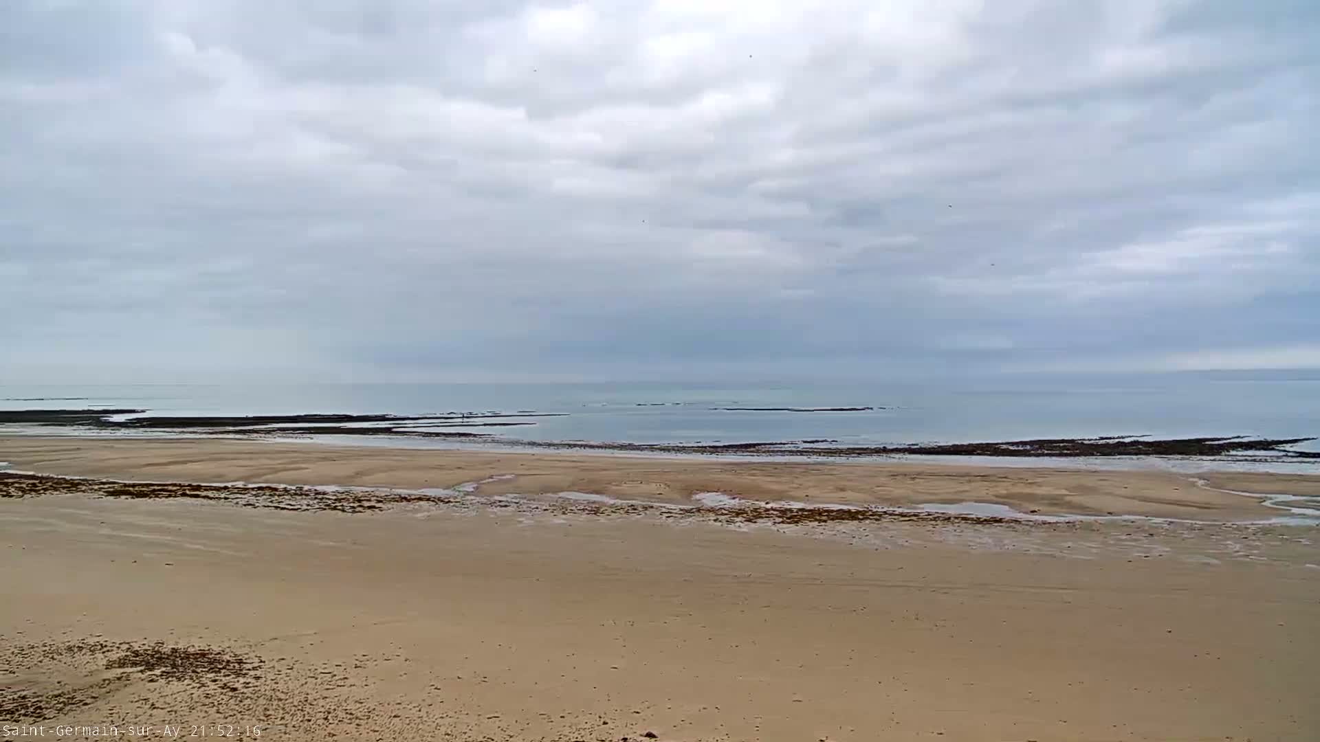 A wide sandy beach stretches to a calm ocean under a cloudy sky.