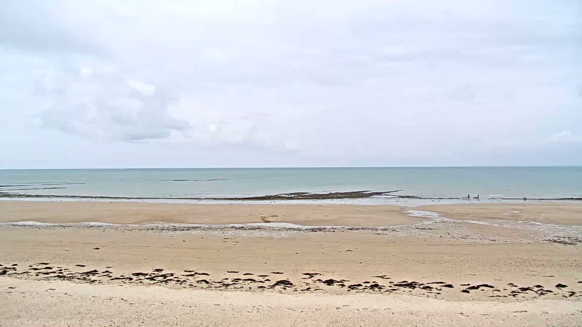 A wide sandy beach stretches to a calm, light-green ocean under a mostly cloudy sky.