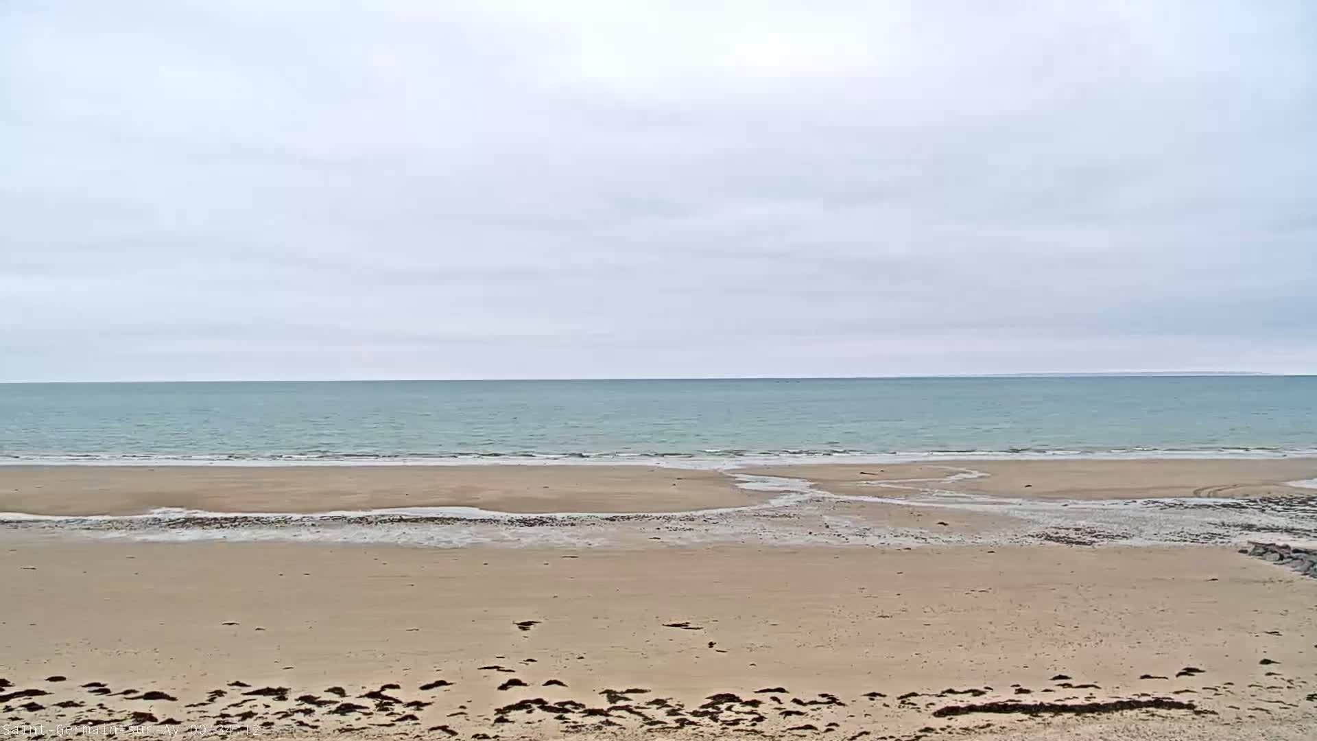 A sandy beach stretches to a calm, light-blue ocean under an overcast sky.