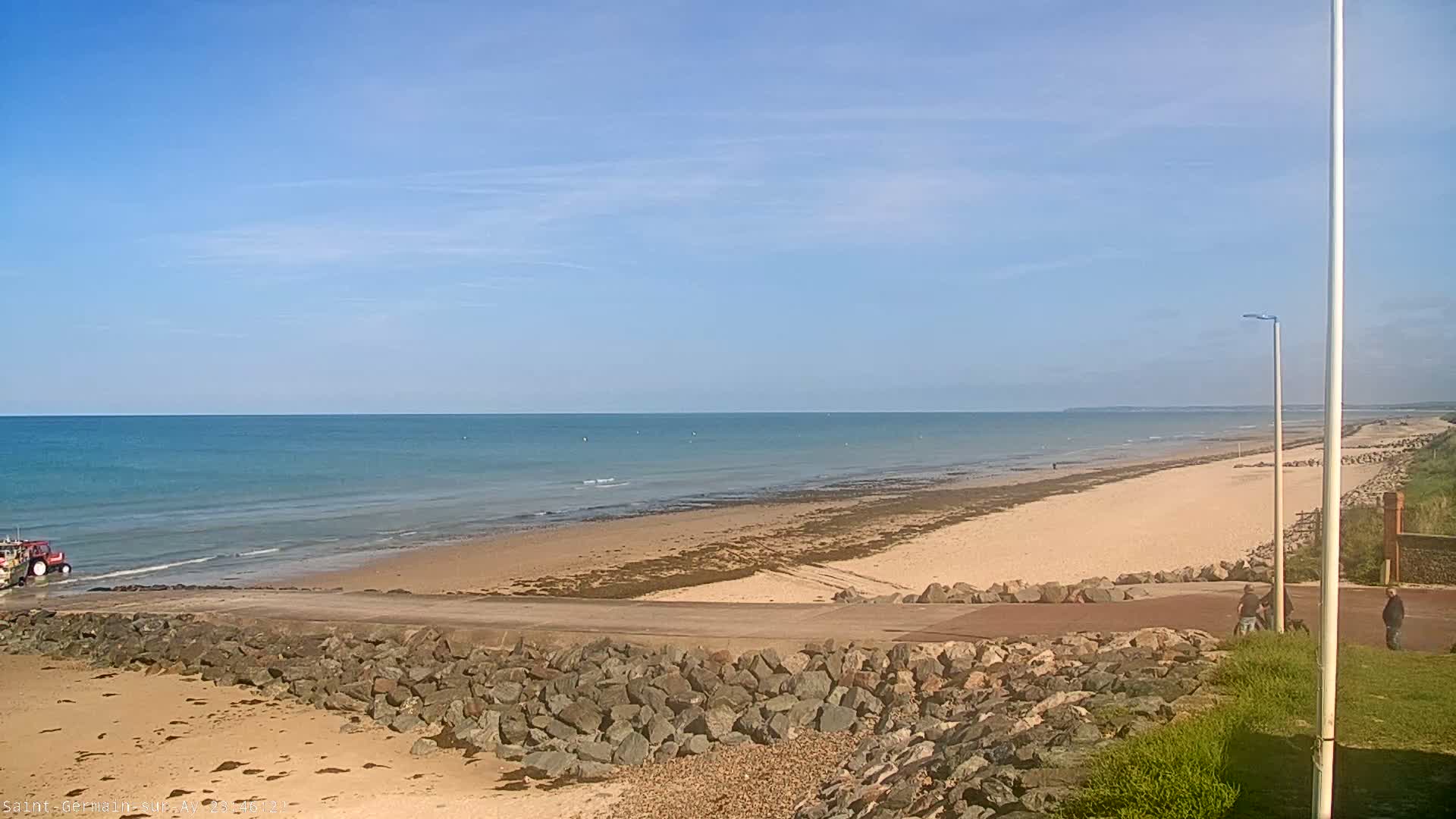 A tractor is on a sandy beach next to calm ocean water under a clear blue sky.