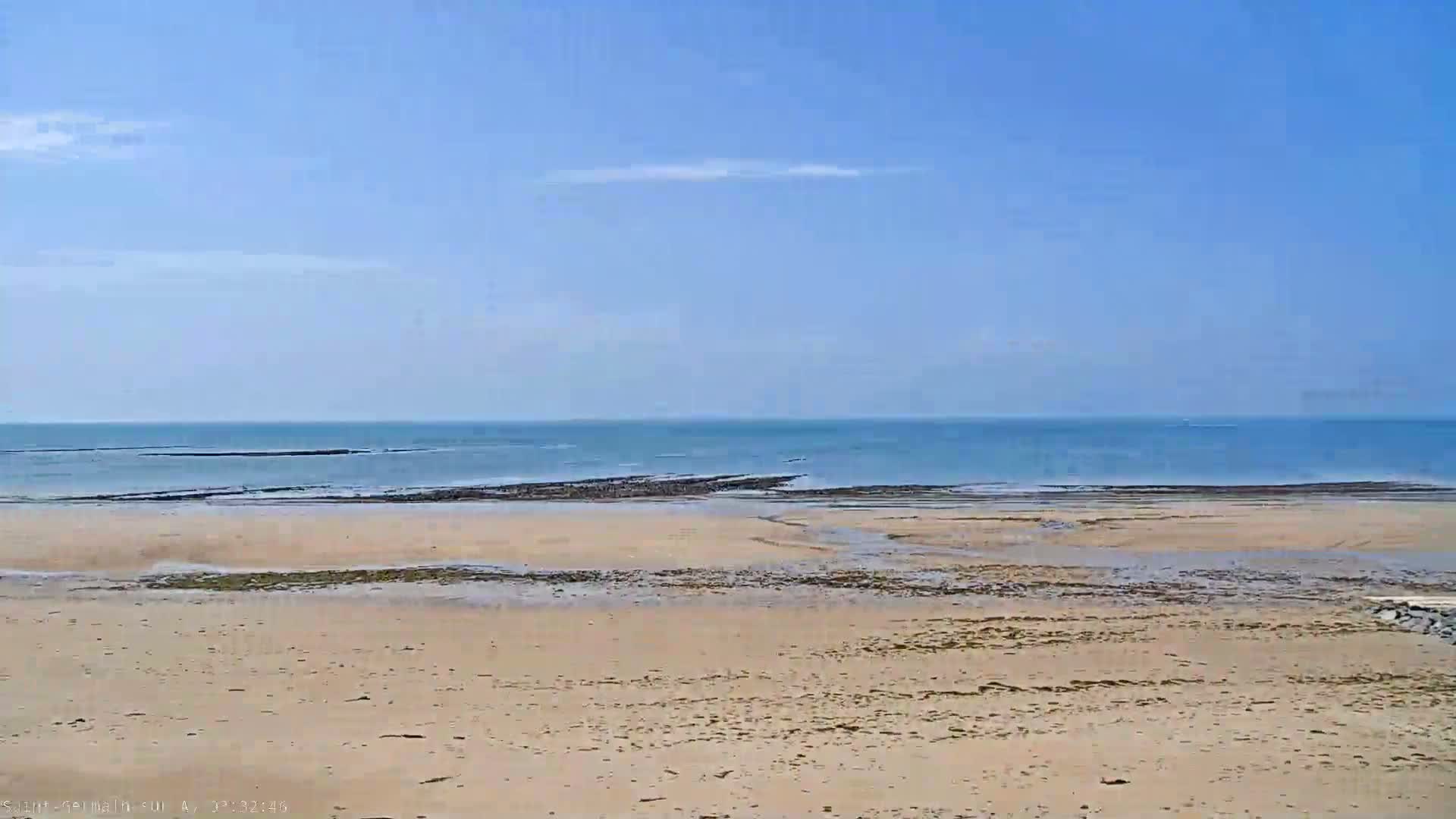 A sandy beach stretches to a calm, blue ocean under a clear, bright sky.