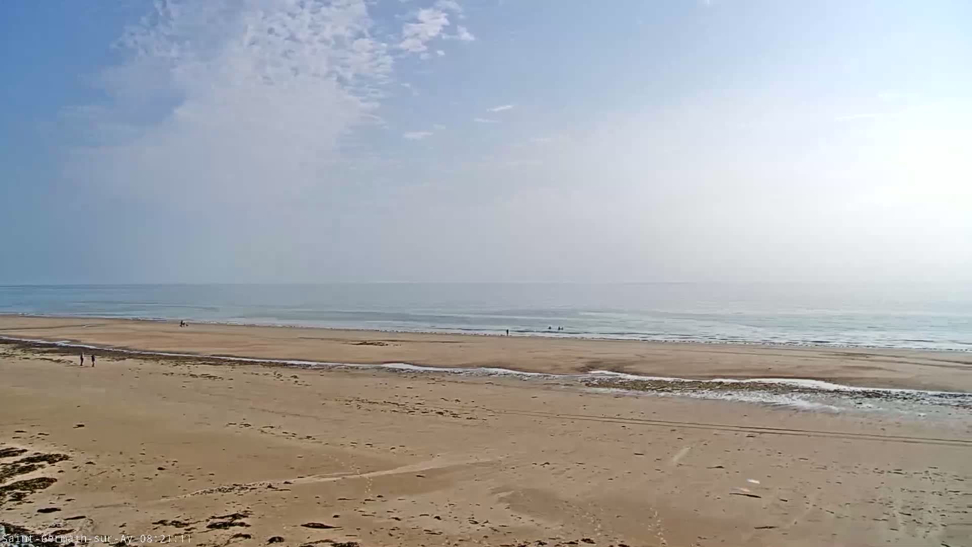 A wide sandy beach stretches to a calm ocean under a mostly clear, slightly hazy sky.