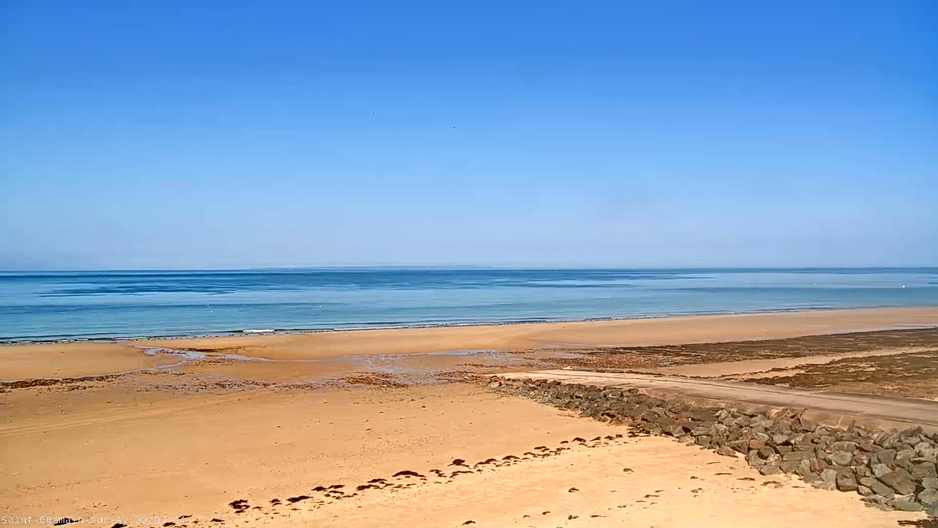 A sandy beach stretches to a calm, light blue ocean under a clear blue sky.