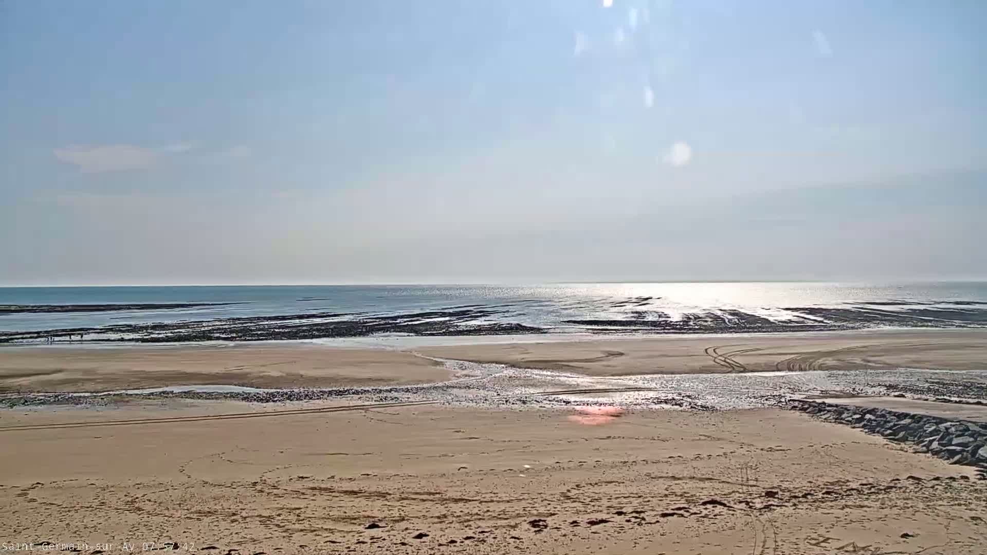 A sandy beach stretches to a calm ocean under a clear, sunny sky.