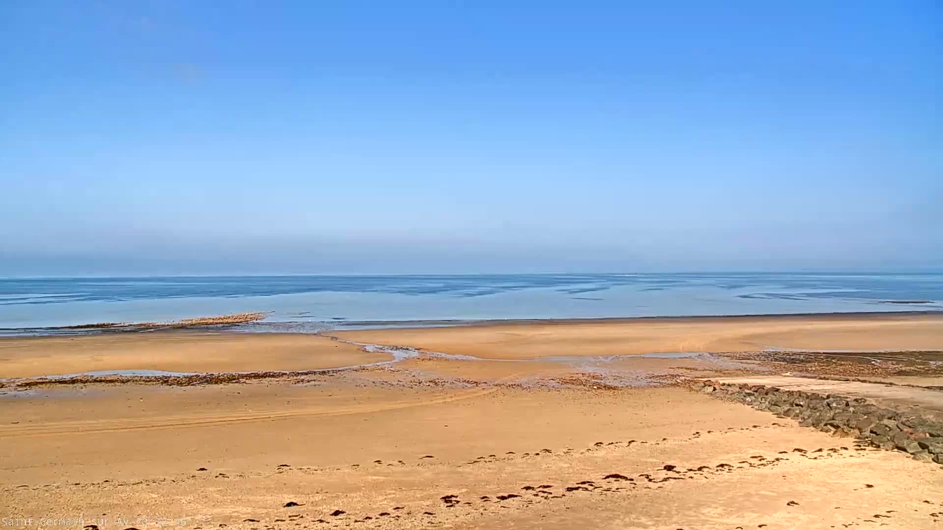 A wide sandy beach stretches to a calm, light-blue ocean under a clear blue sky.