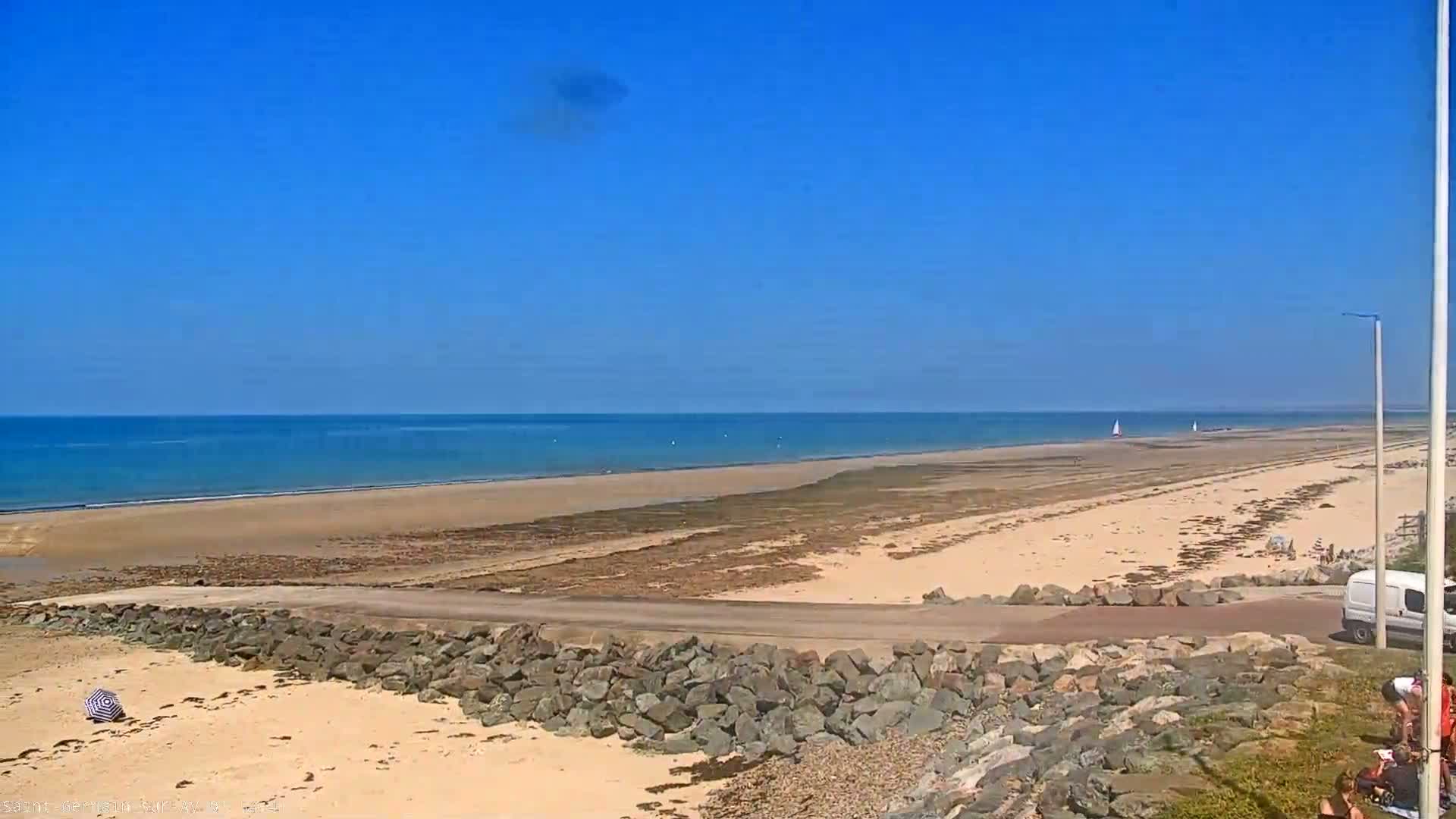 A wide sandy beach stretches to a calm, blue ocean under a clear blue sky.
