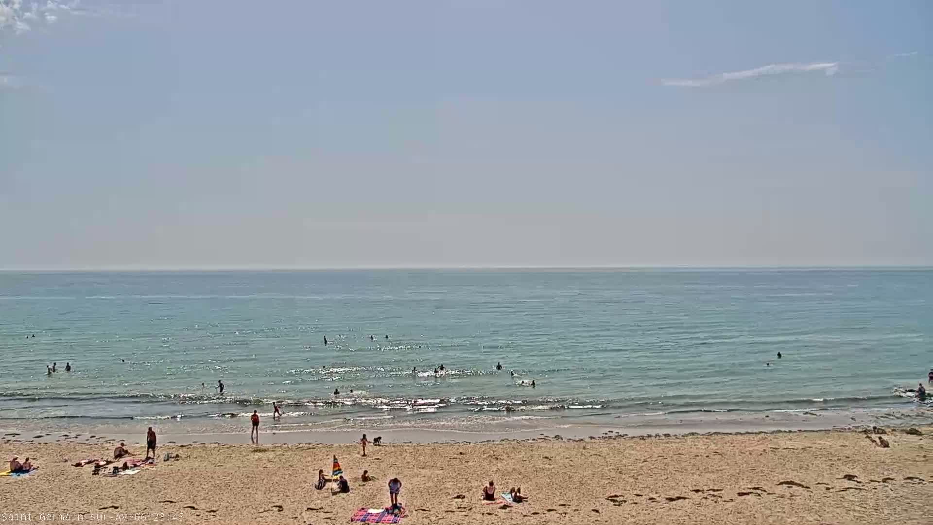 A sandy beach with people swimming and relaxing on a sunny day with a calm, light-blue ocean.