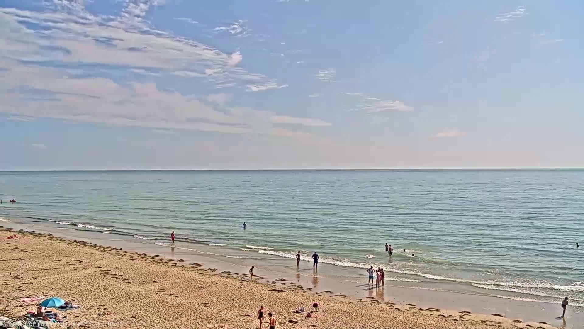 A sandy beach with a few people swimming and relaxing under a partly cloudy sky.