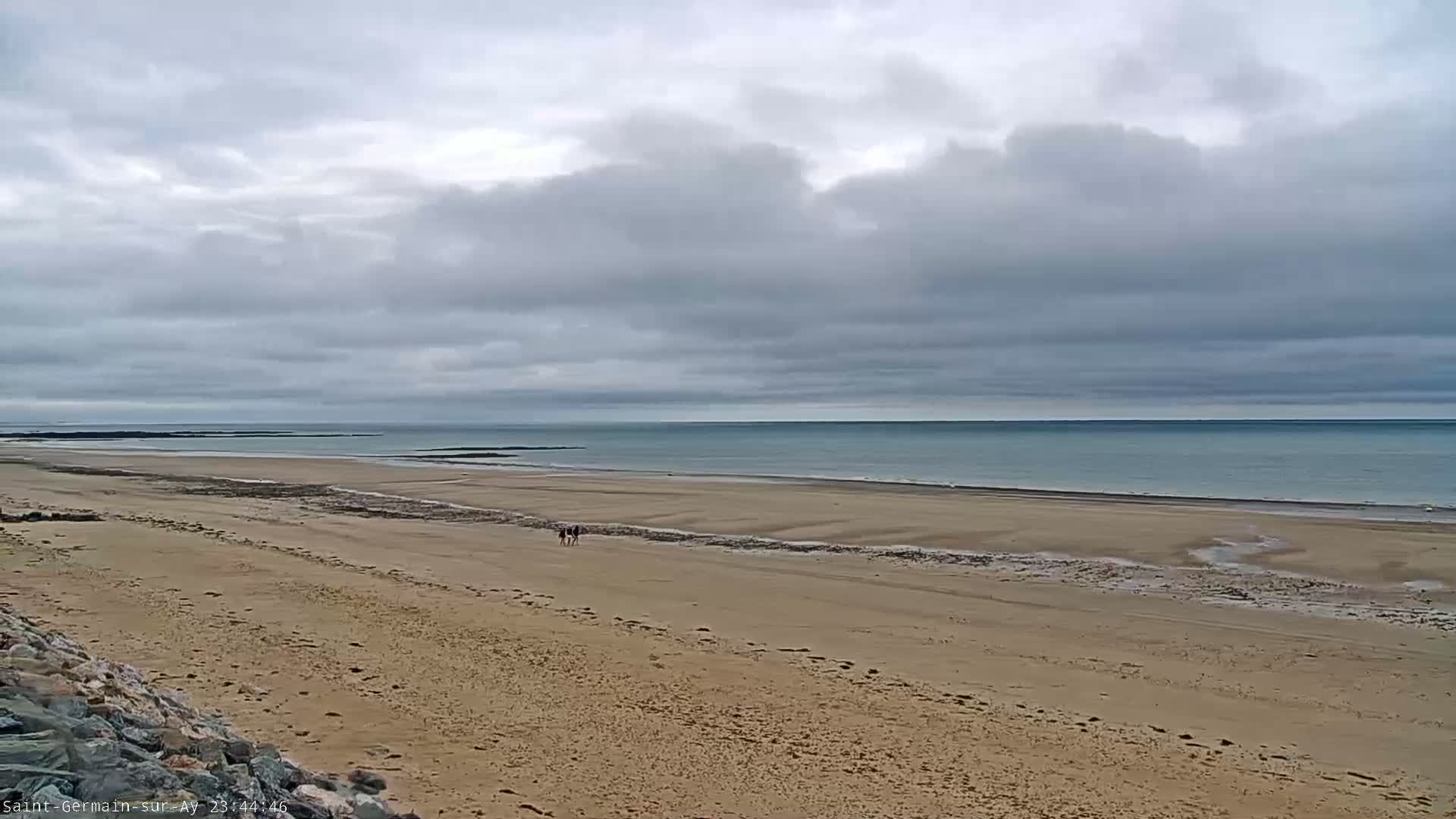 A wide sandy beach stretches to a calm ocean under a cloudy sky.
