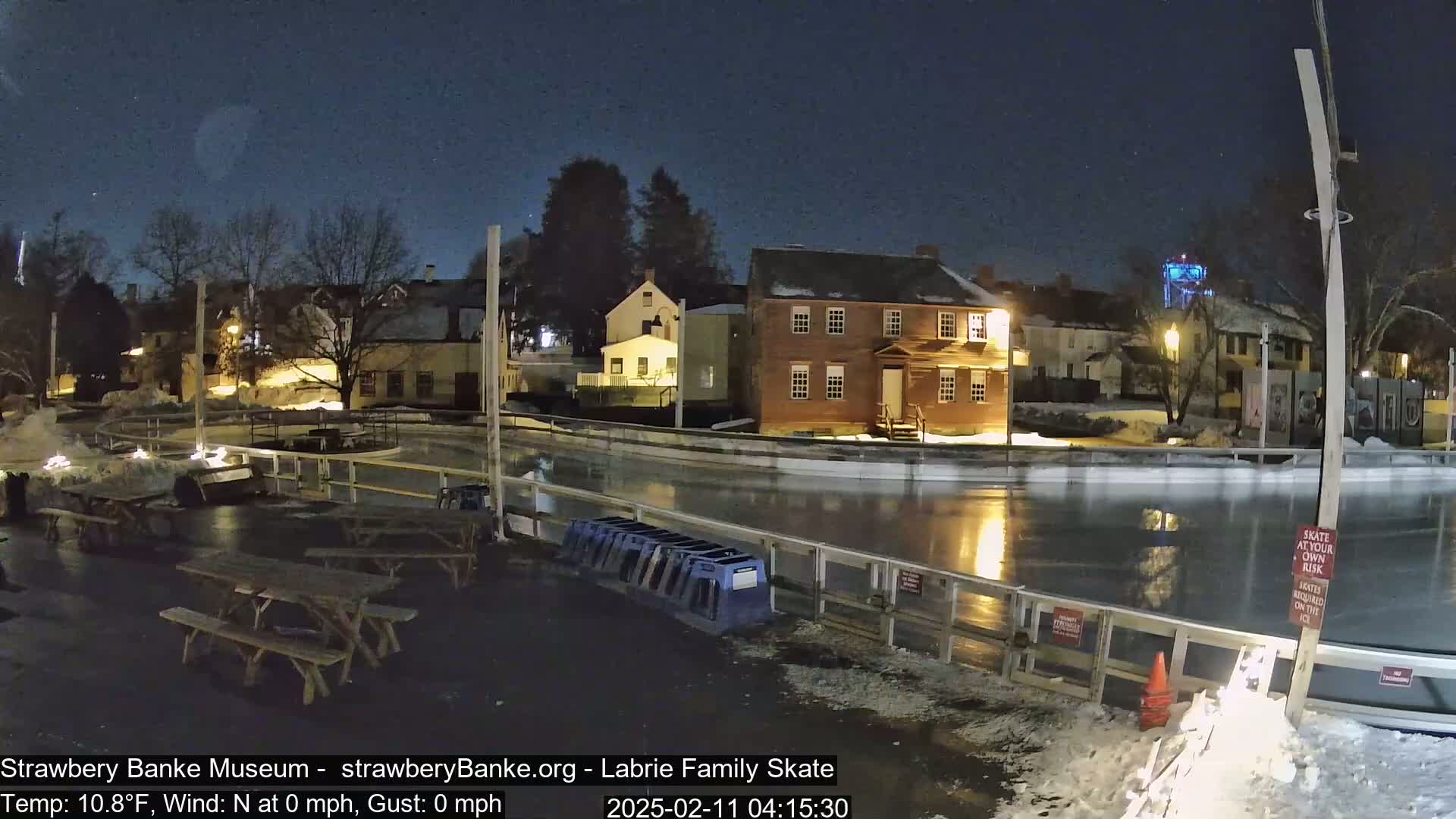 A nighttime view of an outdoor ice rink next to historic buildings under a clear, starry sky.