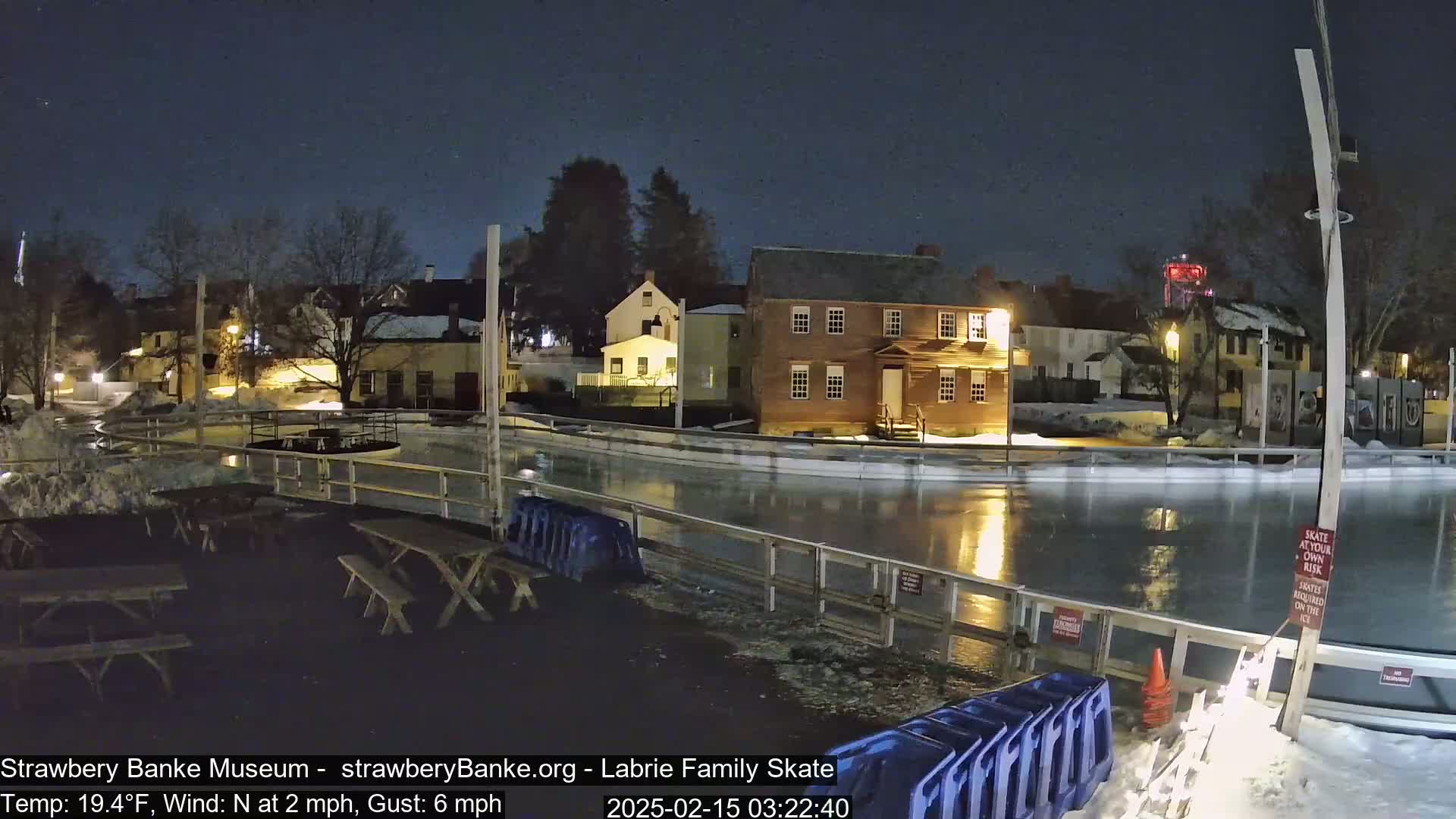 A nighttime view of an outdoor ice skating rink next to illuminated buildings under a clear sky.