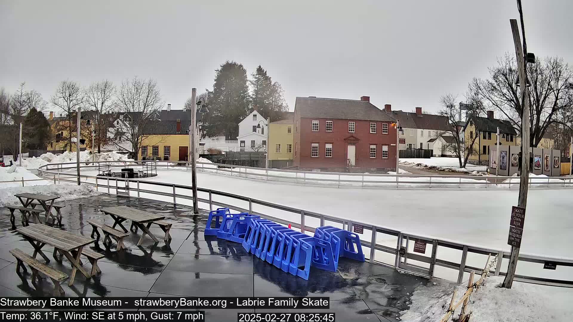 An outdoor ice skating rink is surrounded by historical buildings on a cold, overcast day with a southeasterly wind.