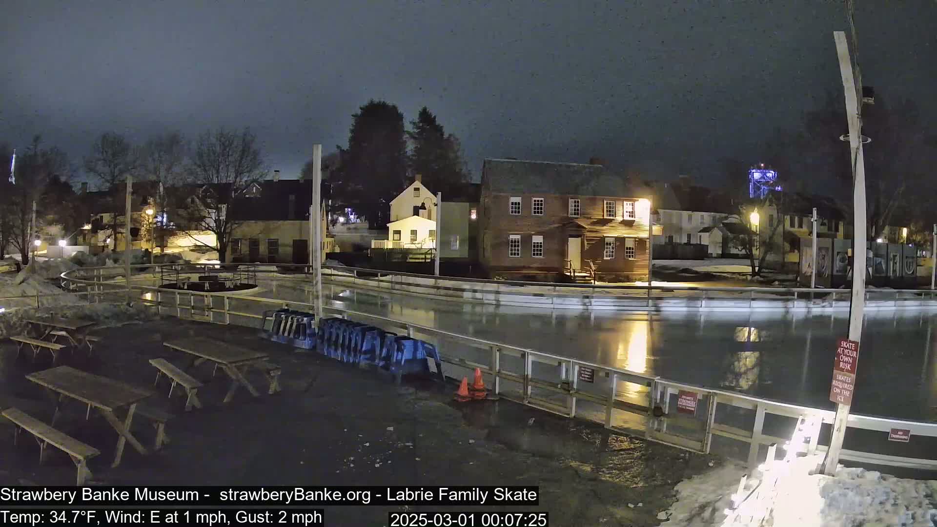 A nighttime view of an outdoor ice rink next to several buildings, with a calm, chilly atmosphere.