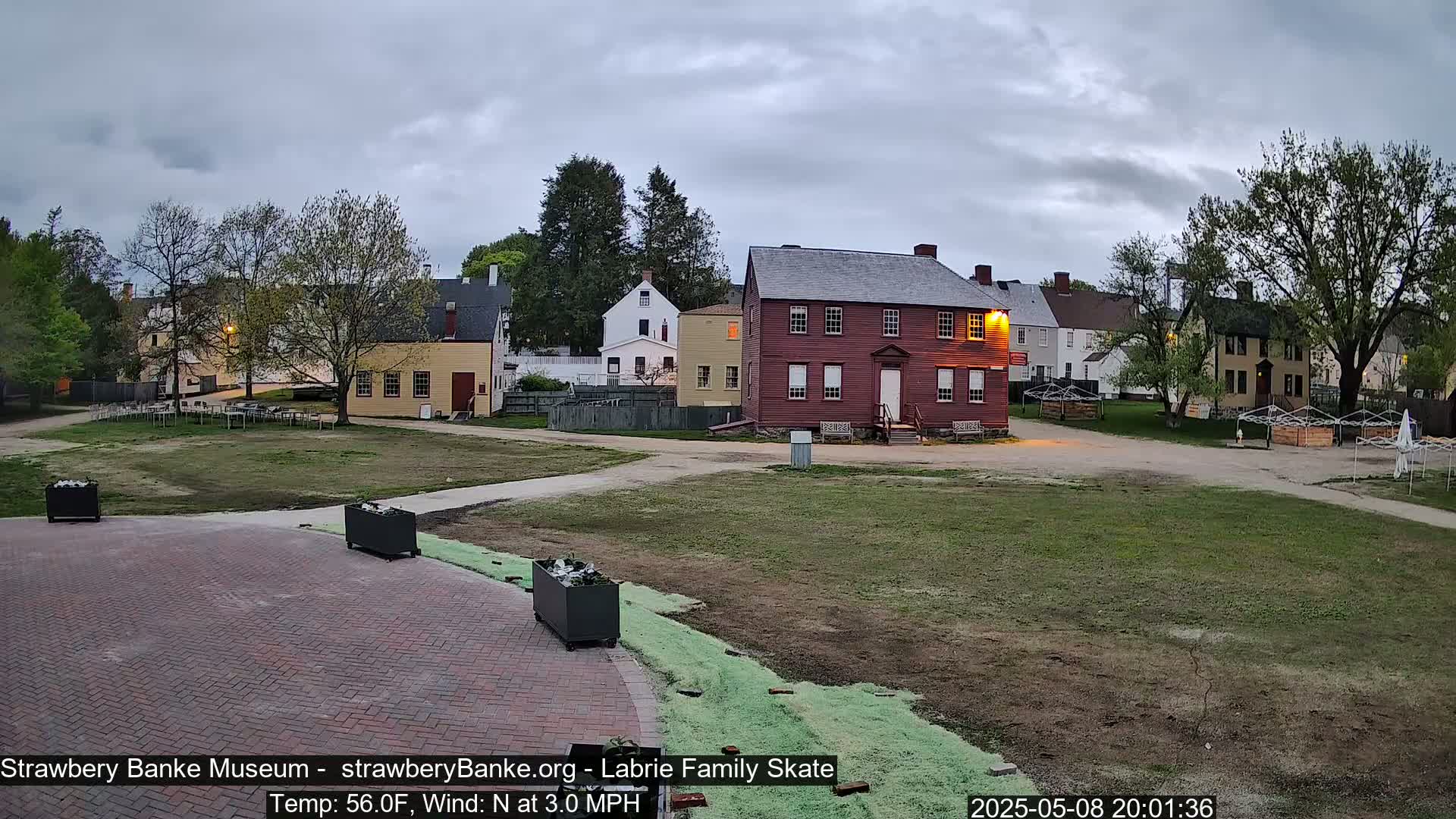 A brick courtyard overlooks several historic-looking buildings under a cloudy evening sky.