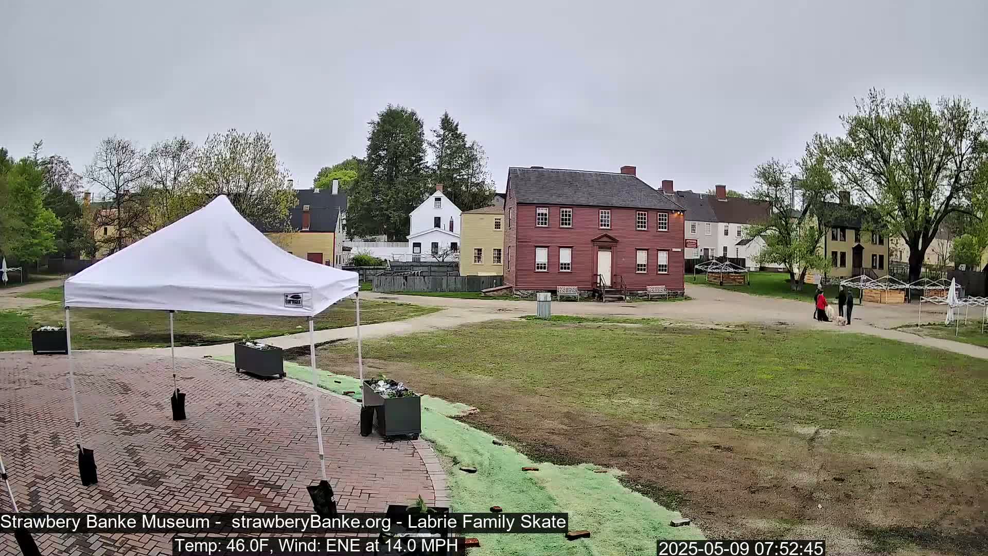 A white canopy tent sits in a brick courtyard next to several historic buildings on an overcast day with a 14 mph wind.