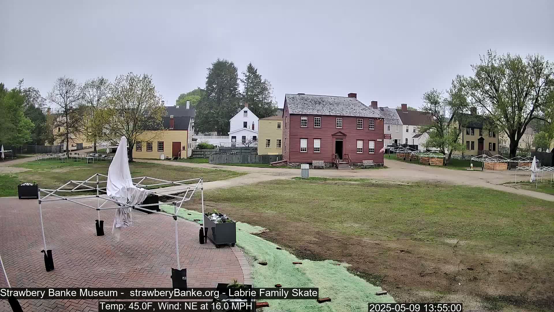 A mostly cloudy day shows several colonial-style buildings and a grassy area with some covered structures and planters.
