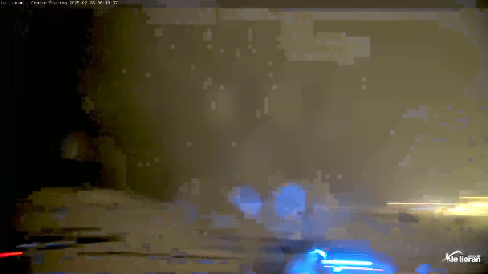 A nighttime, snowy scene shows blurry headlights of vehicles driving on a road.