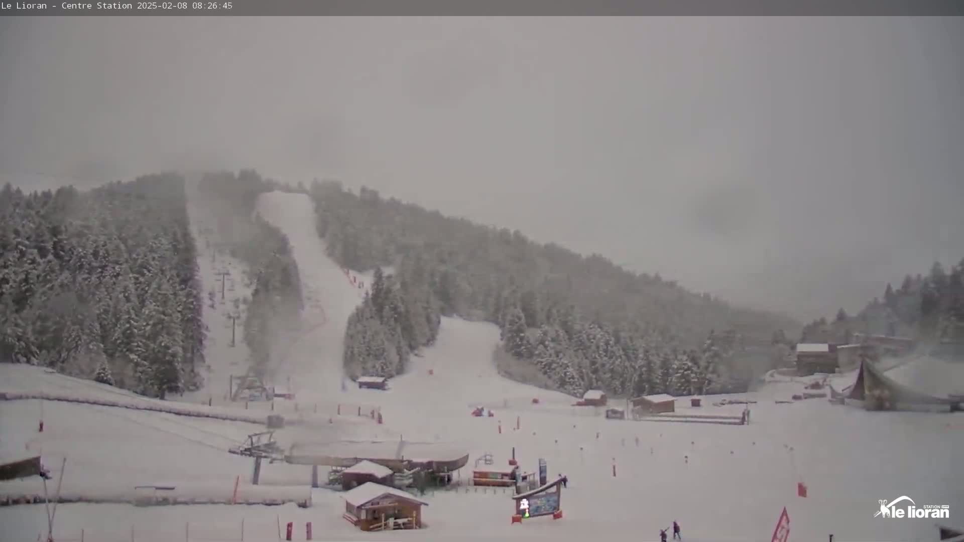A snow-covered ski resort with several ski slopes and small buildings is seen during a heavy snowstorm.