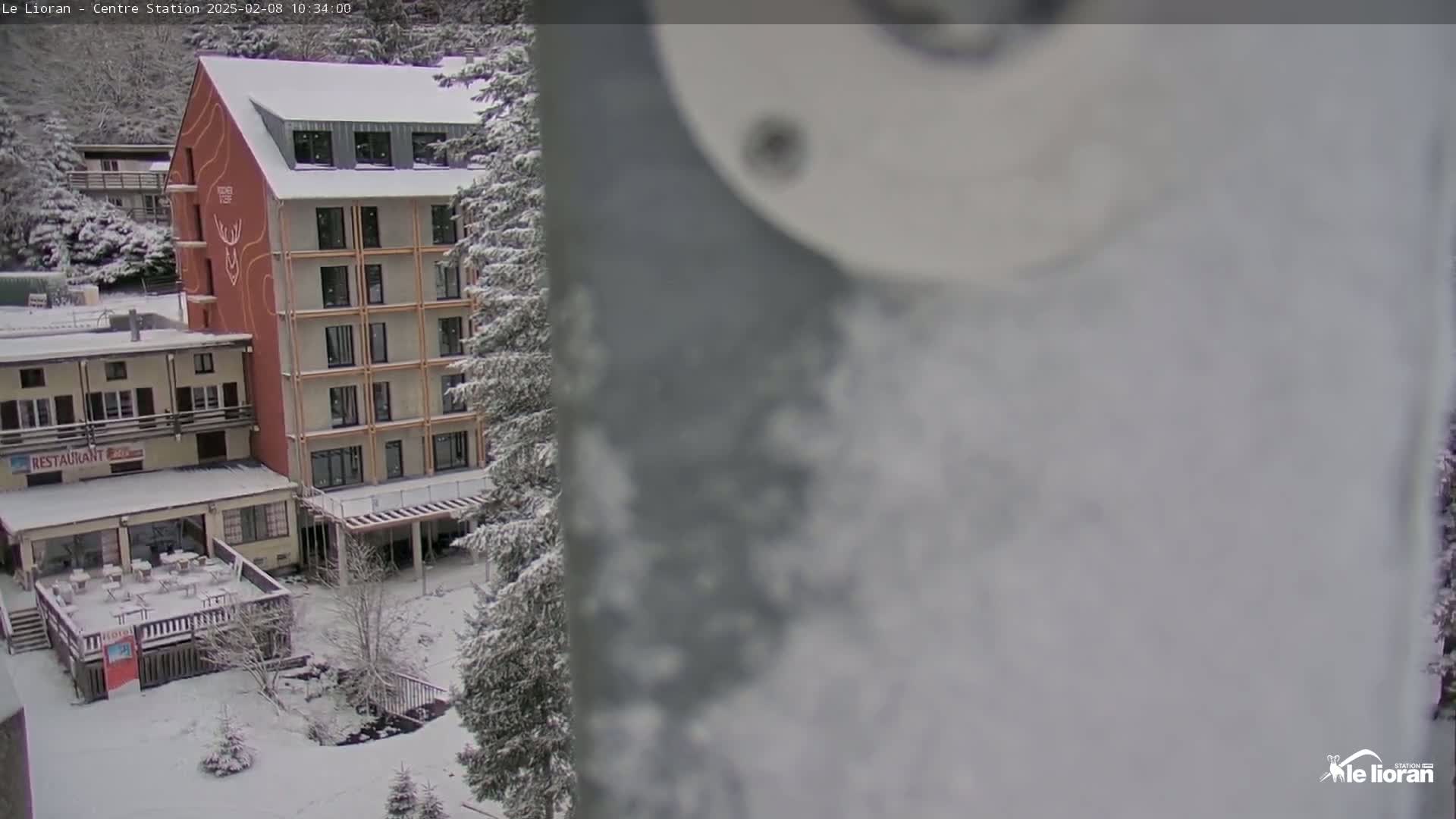A snow-covered scene shows a multi-story building with a restaurant, surrounded by snow-covered trees and ground.