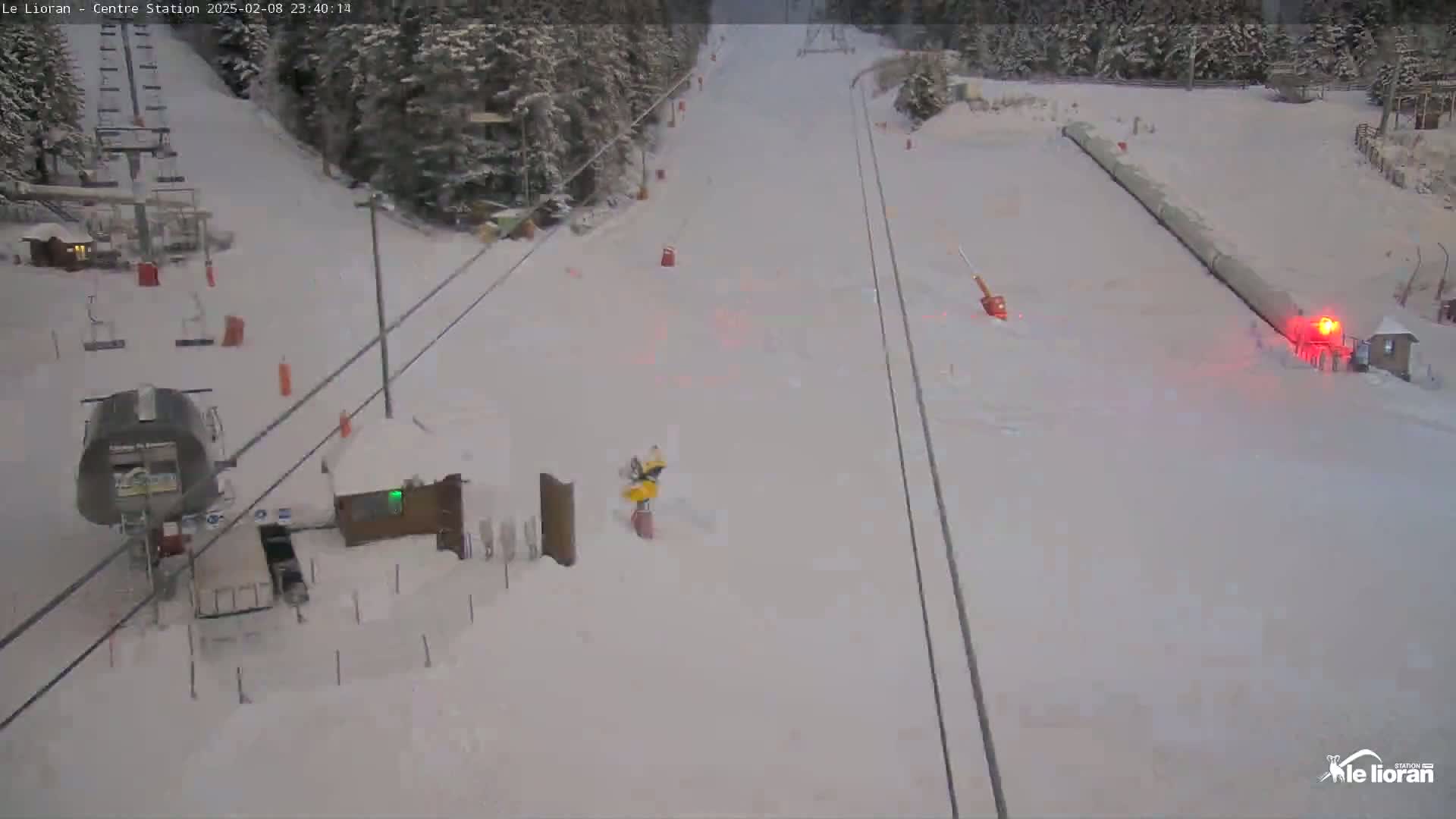 A snow-covered ski slope with a chairlift and snow-covered trees in the background under a cloudy sky.