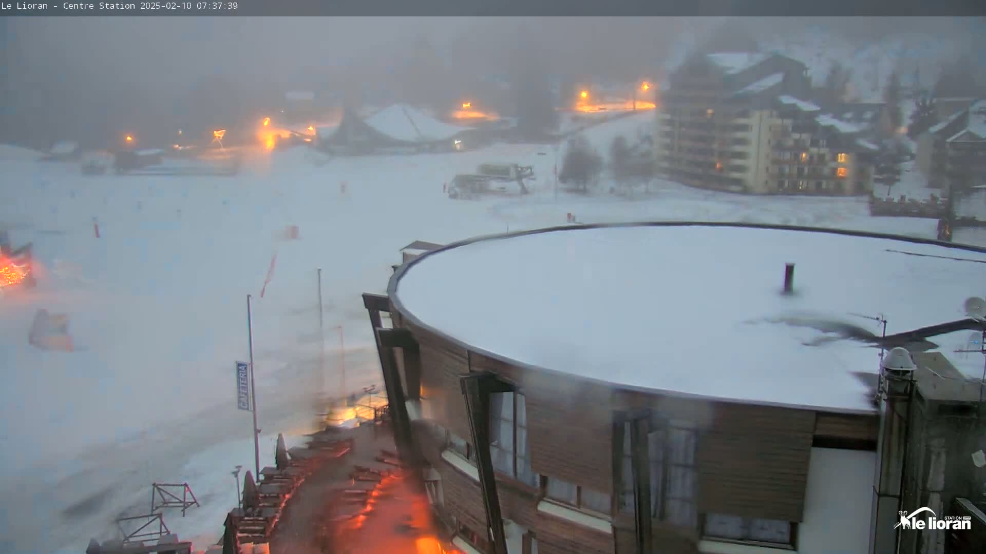 A snow-covered ski resort with a round building in the foreground during a heavy snowstorm.