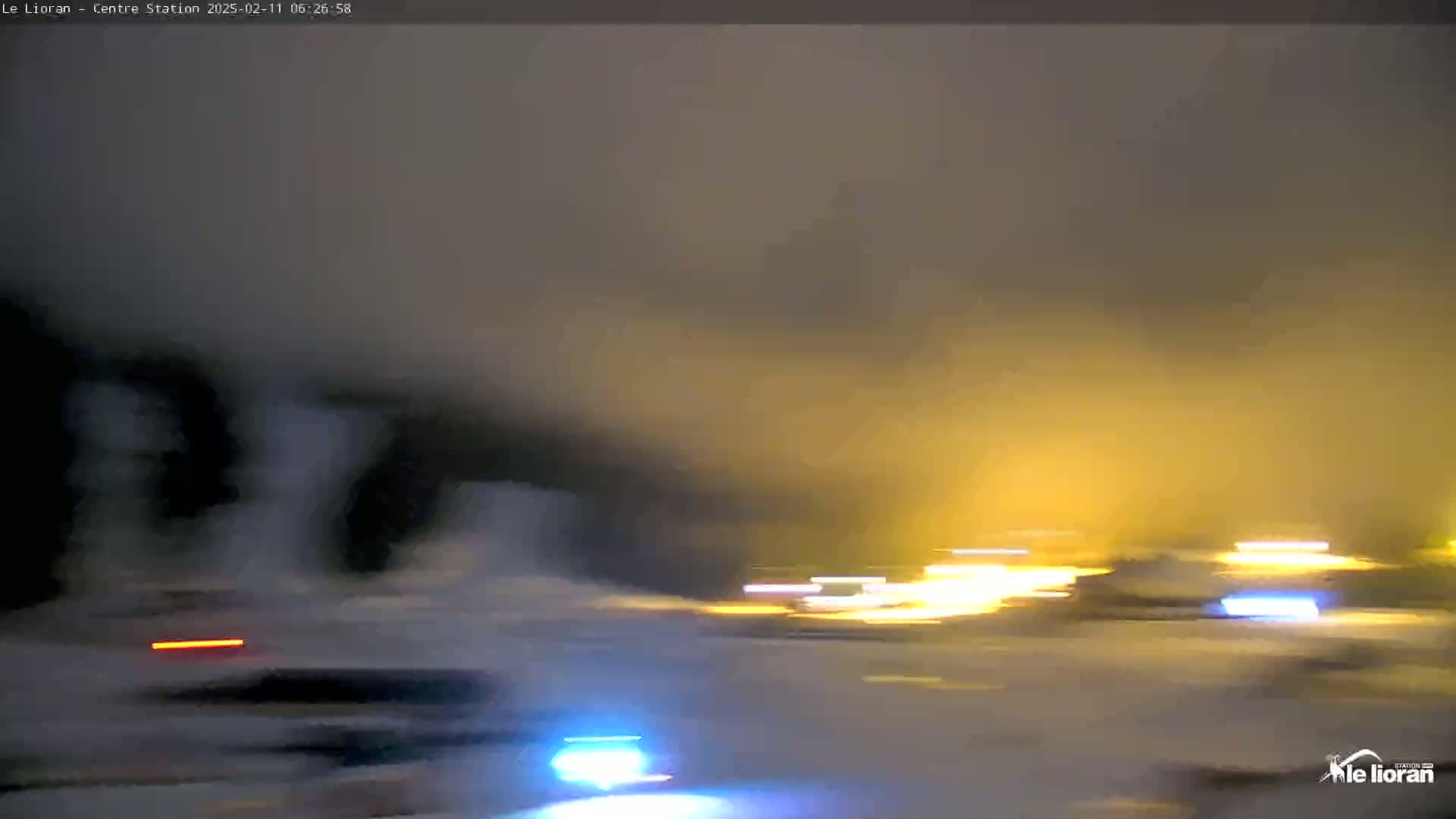A blurry night scene shows bright lights from vehicles in the distance and a hazy, possibly snowy or foggy, atmosphere.