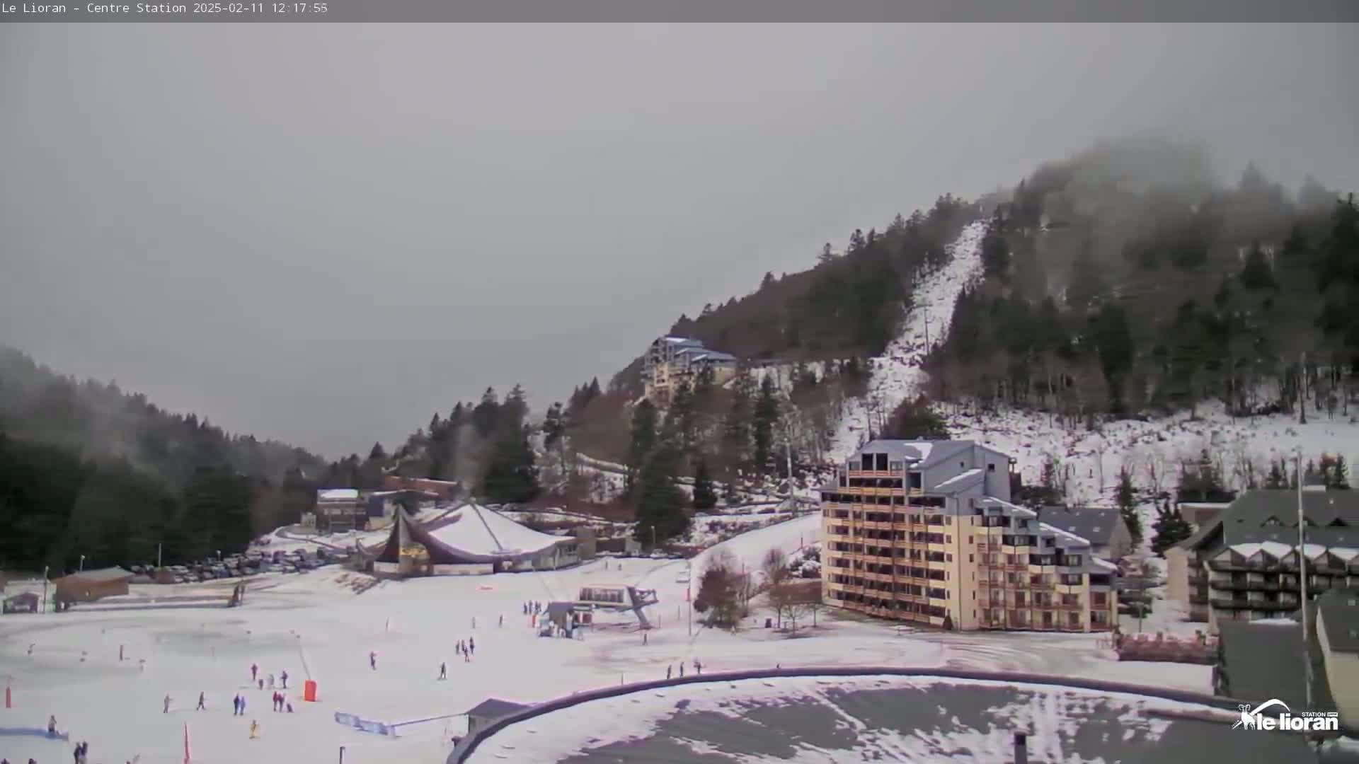 A snow-covered ski resort with several buildings nestled among wooded hills under an overcast sky.