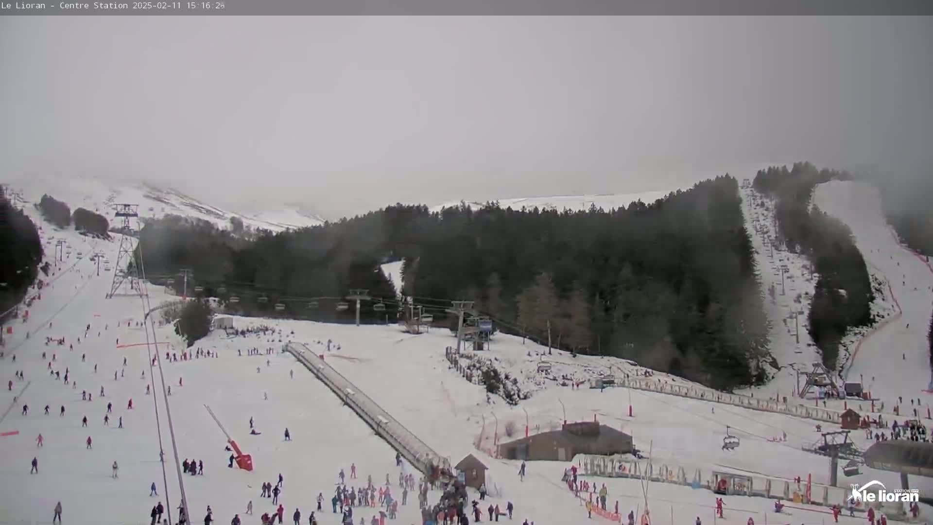 A snowy ski resort with numerous skiers and snowboarders on the slopes under an overcast sky.