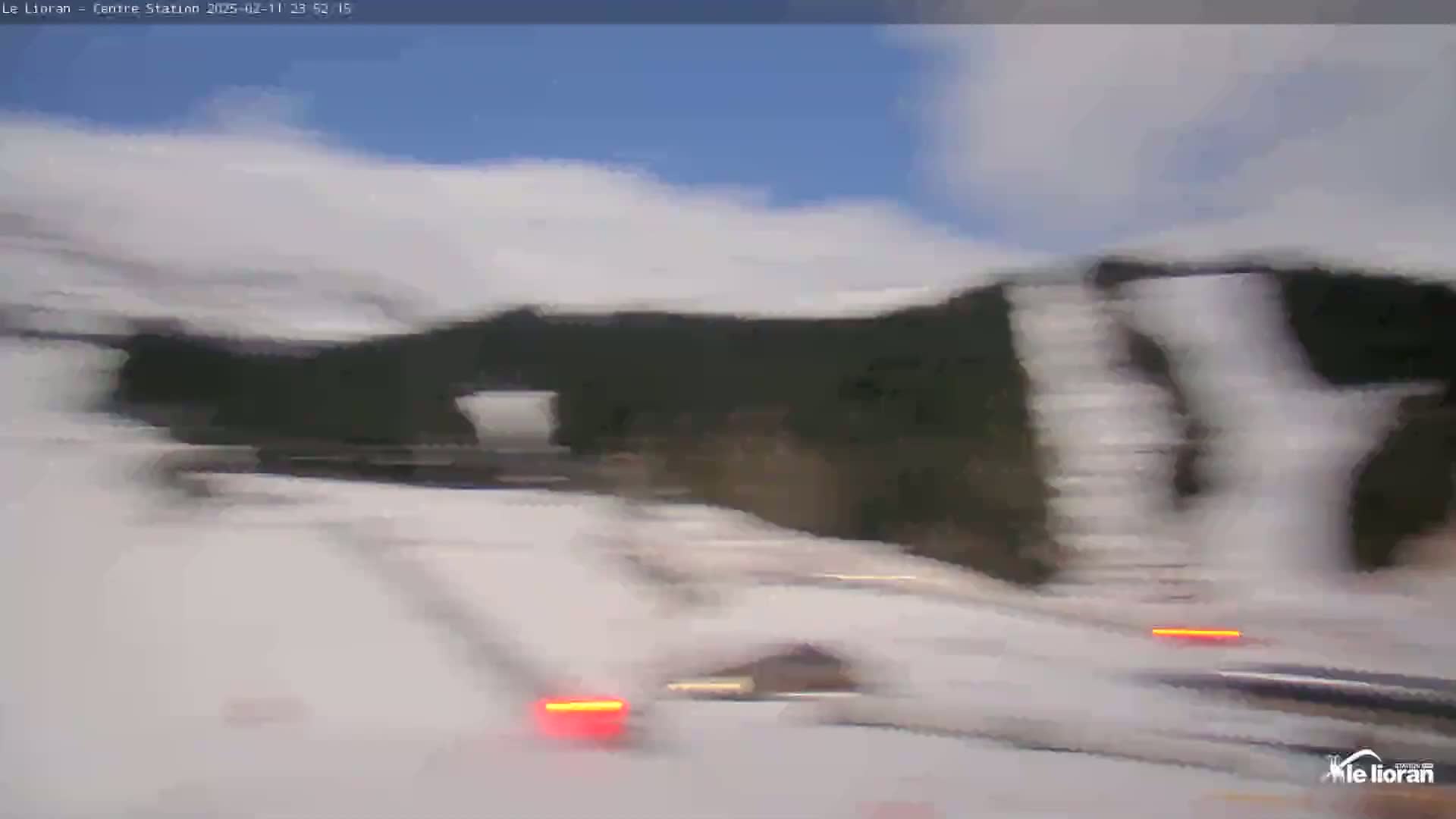 A blurry image shows a snowy, mountainous landscape under a partly cloudy sky.