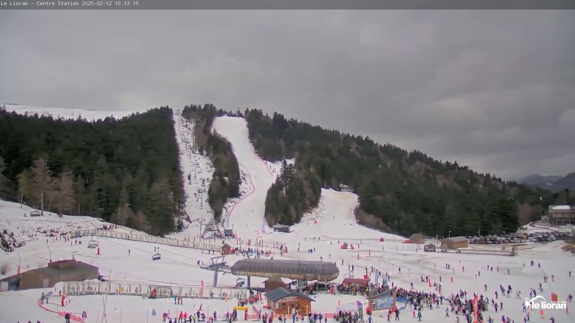 A snow-covered ski resort with many skiers and snowboarders on the slopes under an overcast sky.