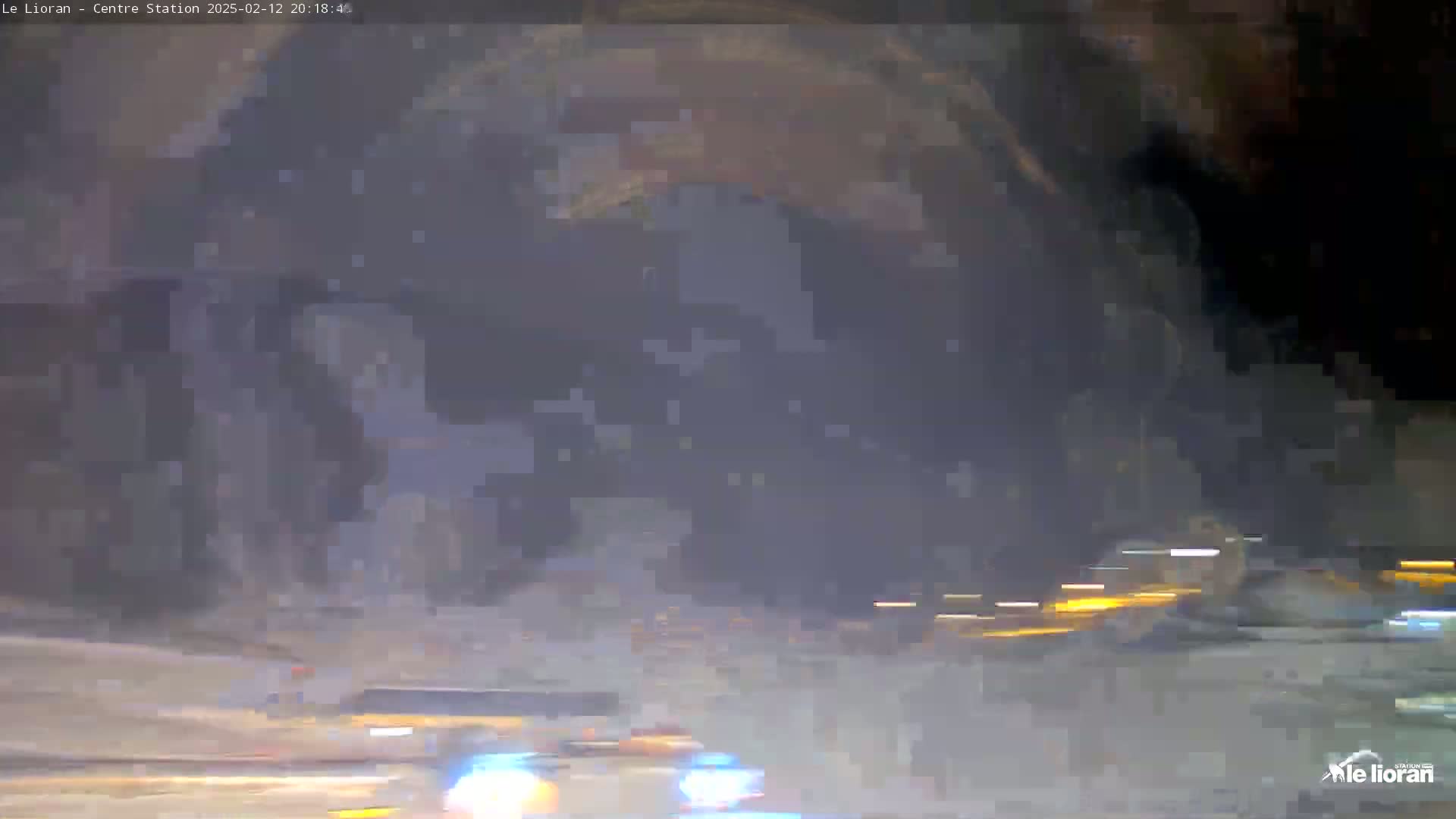 A nighttime, hazy or snowy scene shows blurry, indistinct vehicles moving along a road, with lights visible in the distance.