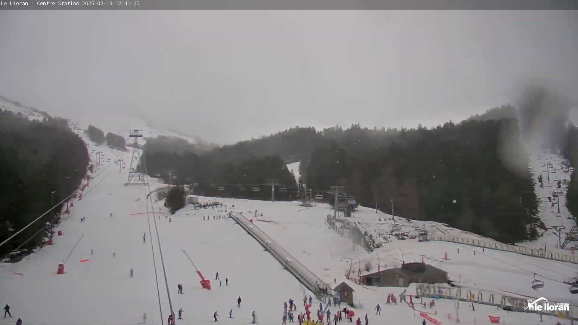 A snowy ski resort with skiers and snowboarders on the slopes under an overcast sky.