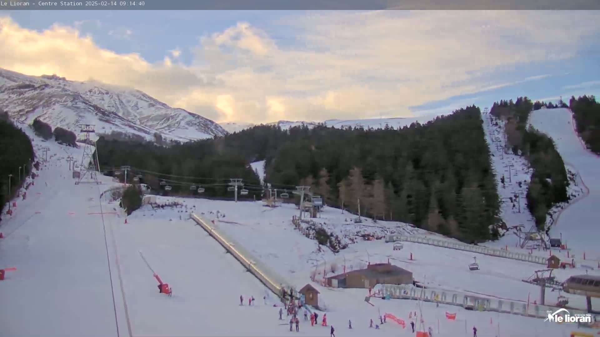 A snow-covered ski resort with several chairlifts and skiers visible under a partly cloudy sky.