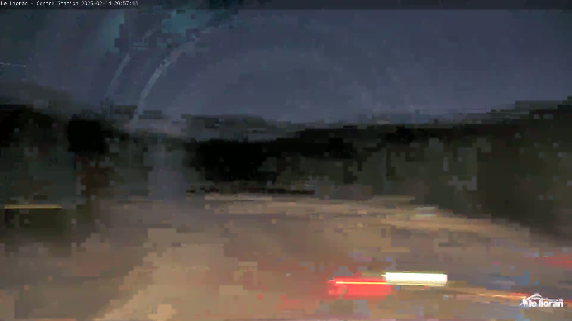 A nighttime, blurry view of a road with vehicle taillights visible in the distance under a dark sky.