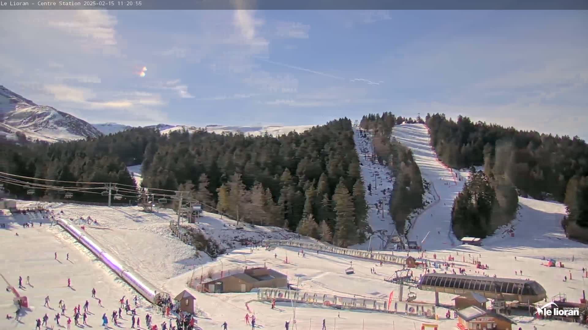 A snowy ski resort with a sunny sky is shown, featuring several ski slopes, lifts, and skiers.