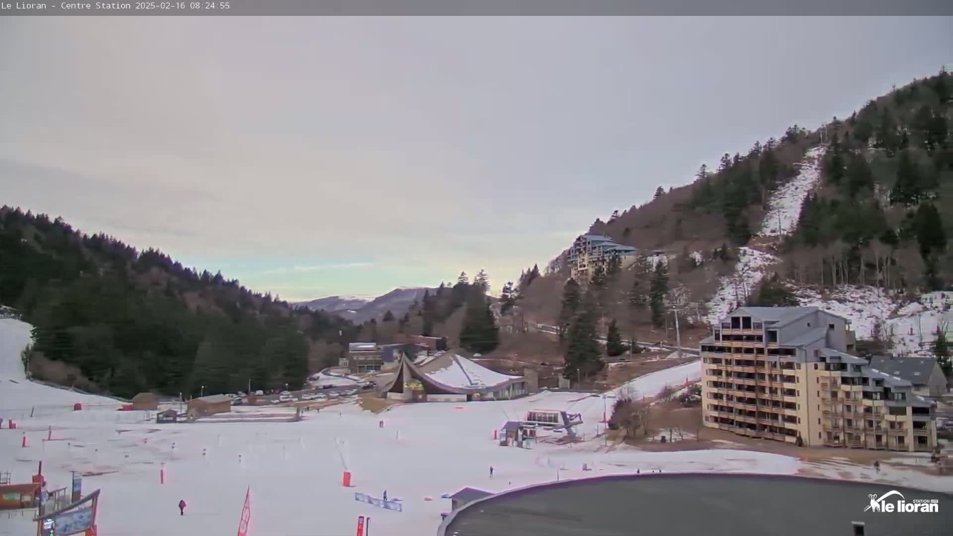A snow-covered ski resort nestled in a valley between snow-dusted mountains under a pale, overcast sky.
