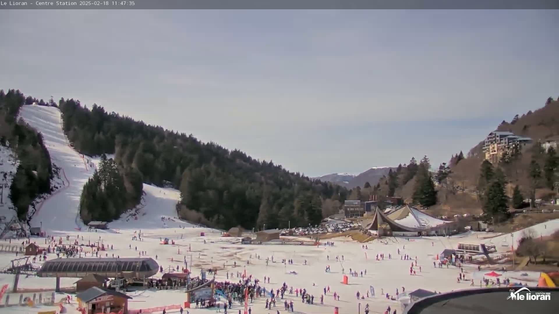 A snowy ski resort with many skiers and snowboarders on the slopes, under a mostly clear sky.