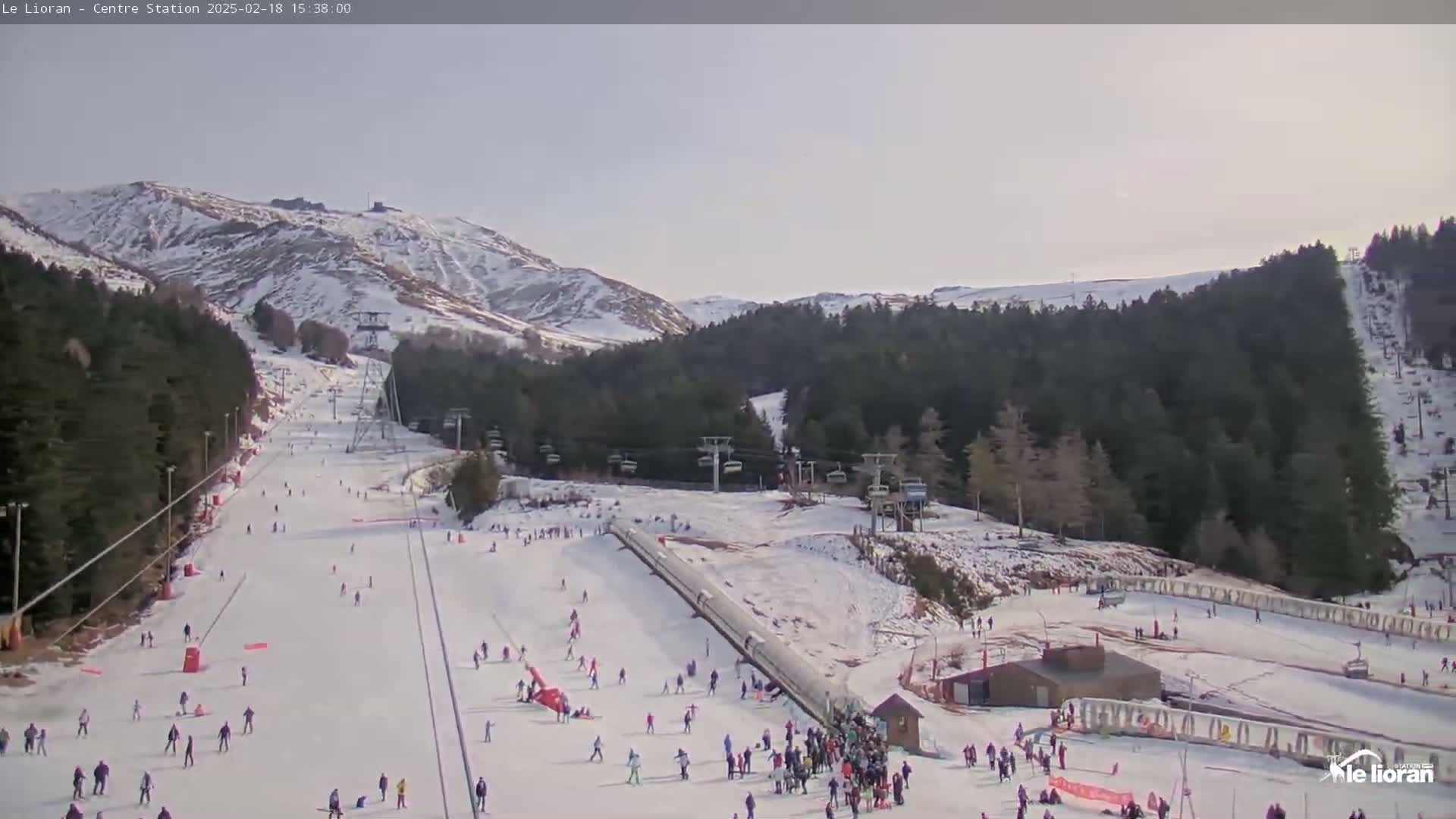 A snowy ski slope with several skiers and snowboarders, ski lifts, and a mountain in the background under a mostly clear sky.