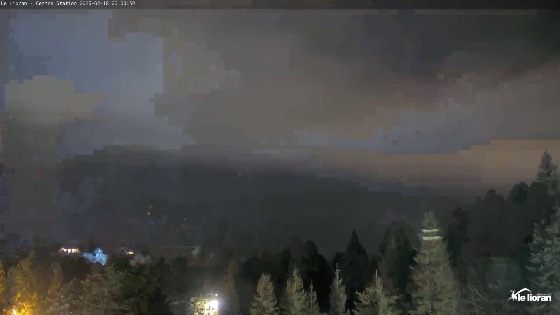 A nighttime view of a mountain range shrouded in a hazy, dark atmosphere, with a line of evergreens in the foreground.