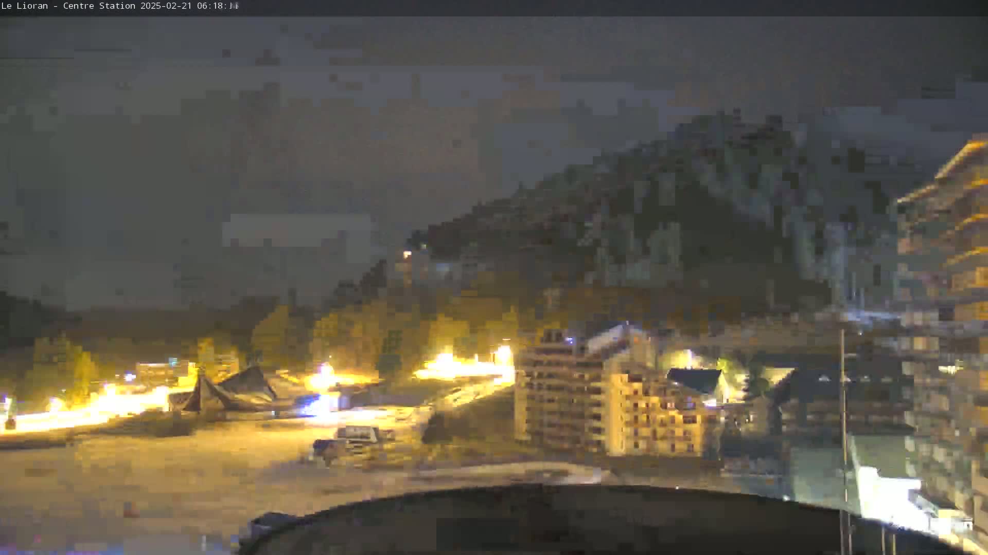 A nighttime view of a snow-covered town nestled at the base of a dark mountain, illuminated by scattered streetlights.