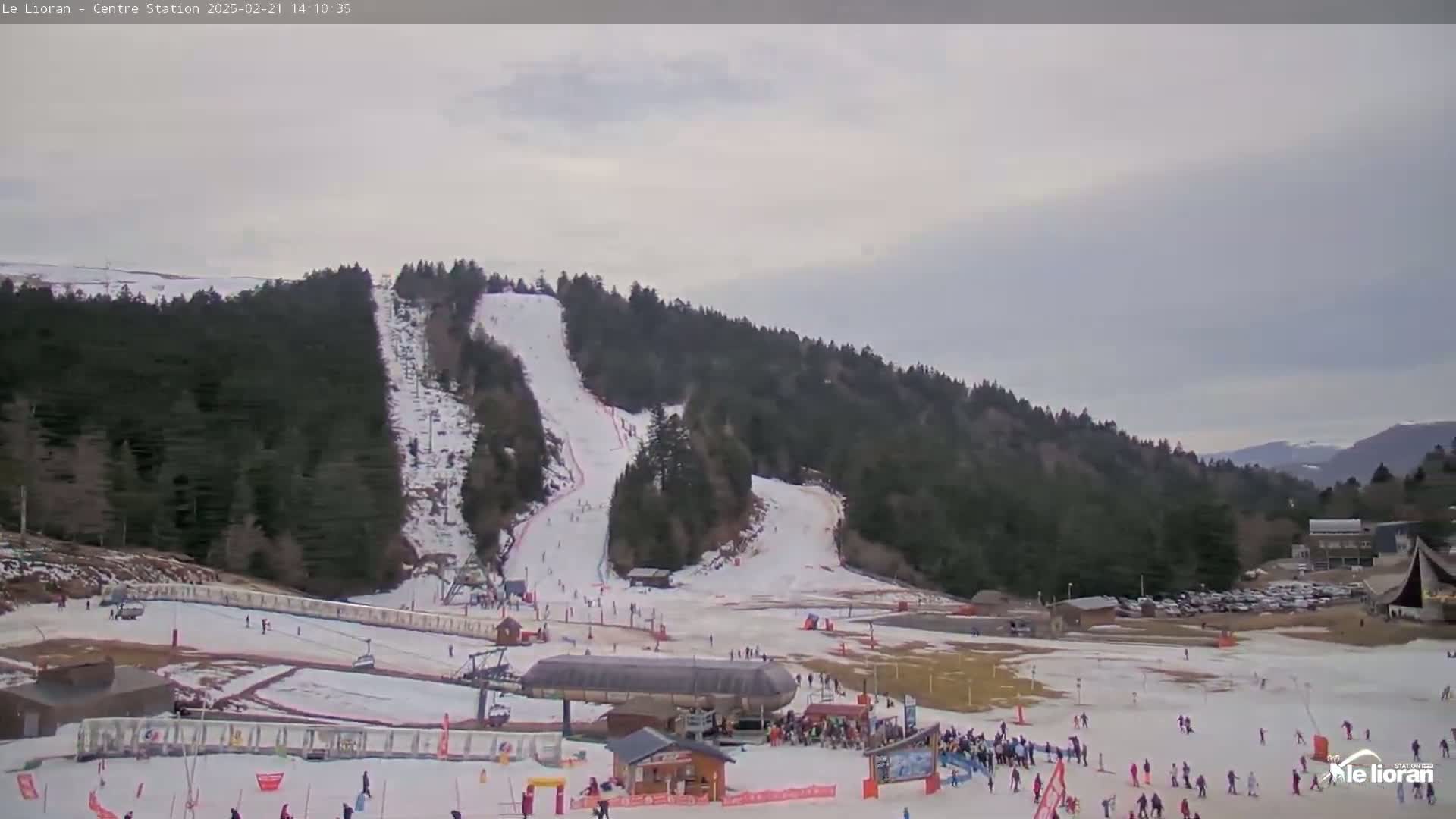 A snow-covered ski slope with skiers and a ski lift on a cloudy day.